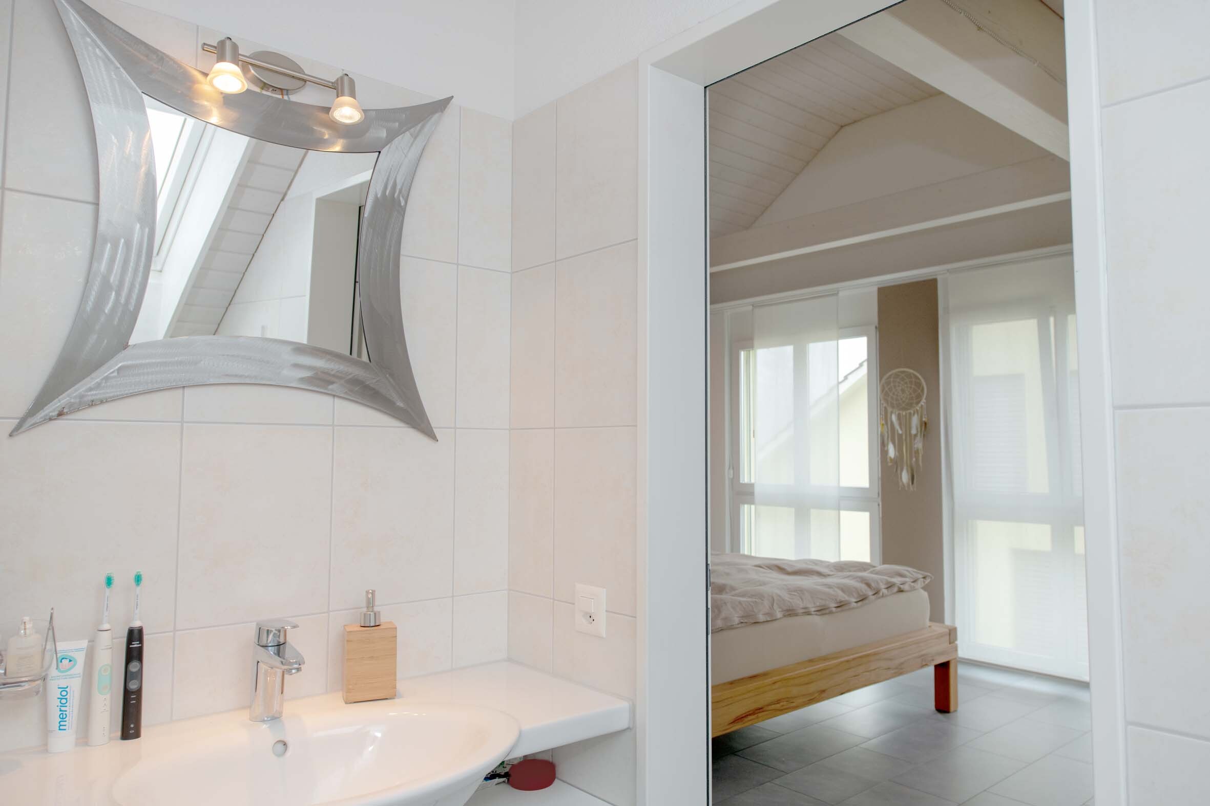 Modernes Badezimmer mit Spiegel und Blick ins Schlafzimmer