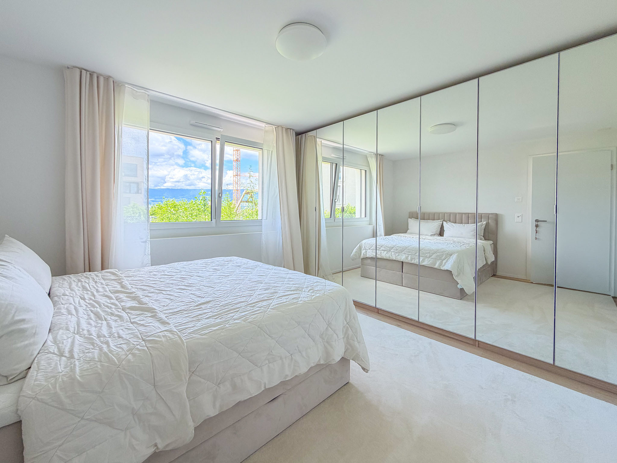 Helles Schlafzimmer mit Spiegelschrank und Fensterblick