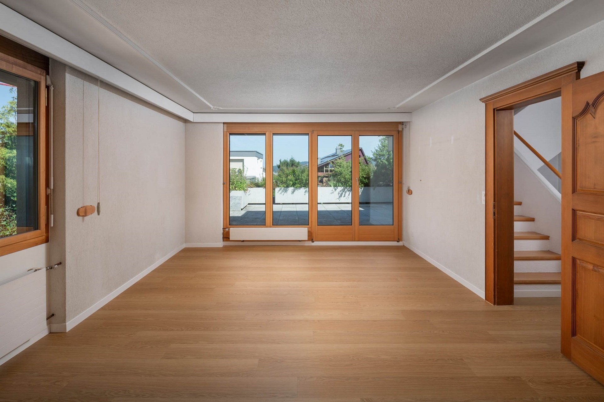 Heller leerer Wohnraum mit Holzfußboden und großer Fensterfront