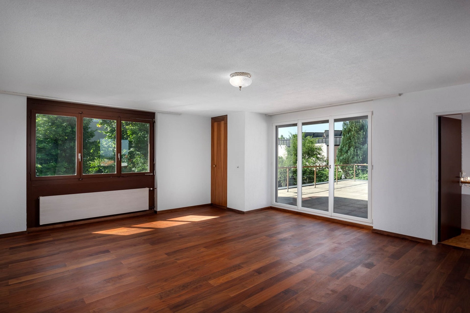 Leerer Wohnraum mit Holzfußboden und großen Fenstern