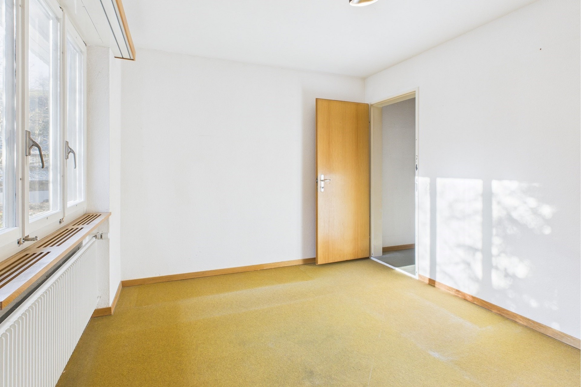Helles, leeres Zimmer mit Fensterfront und offener Tür