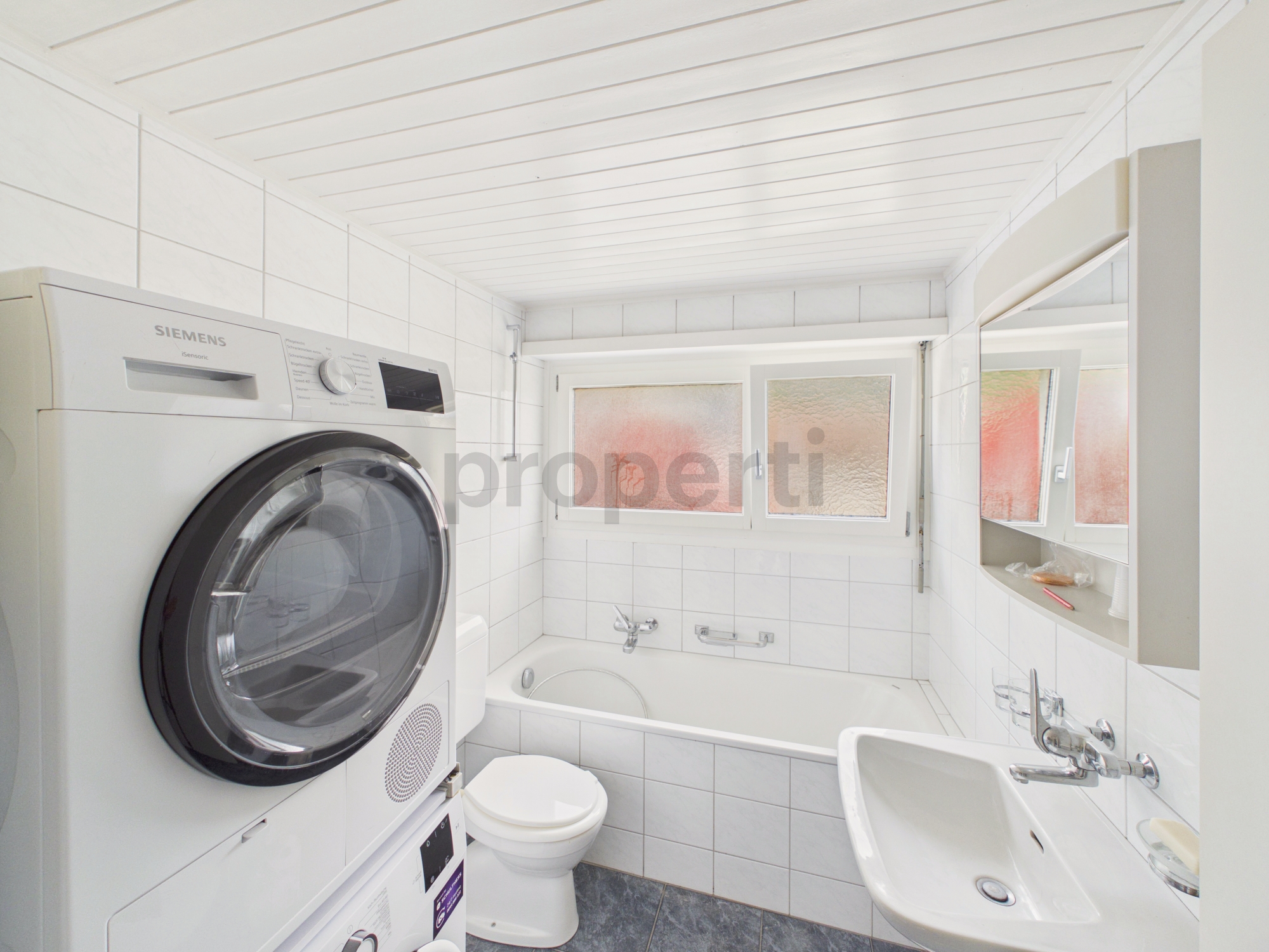 Kleines weißes Badezimmer mit Waschtrockner und Badewanne