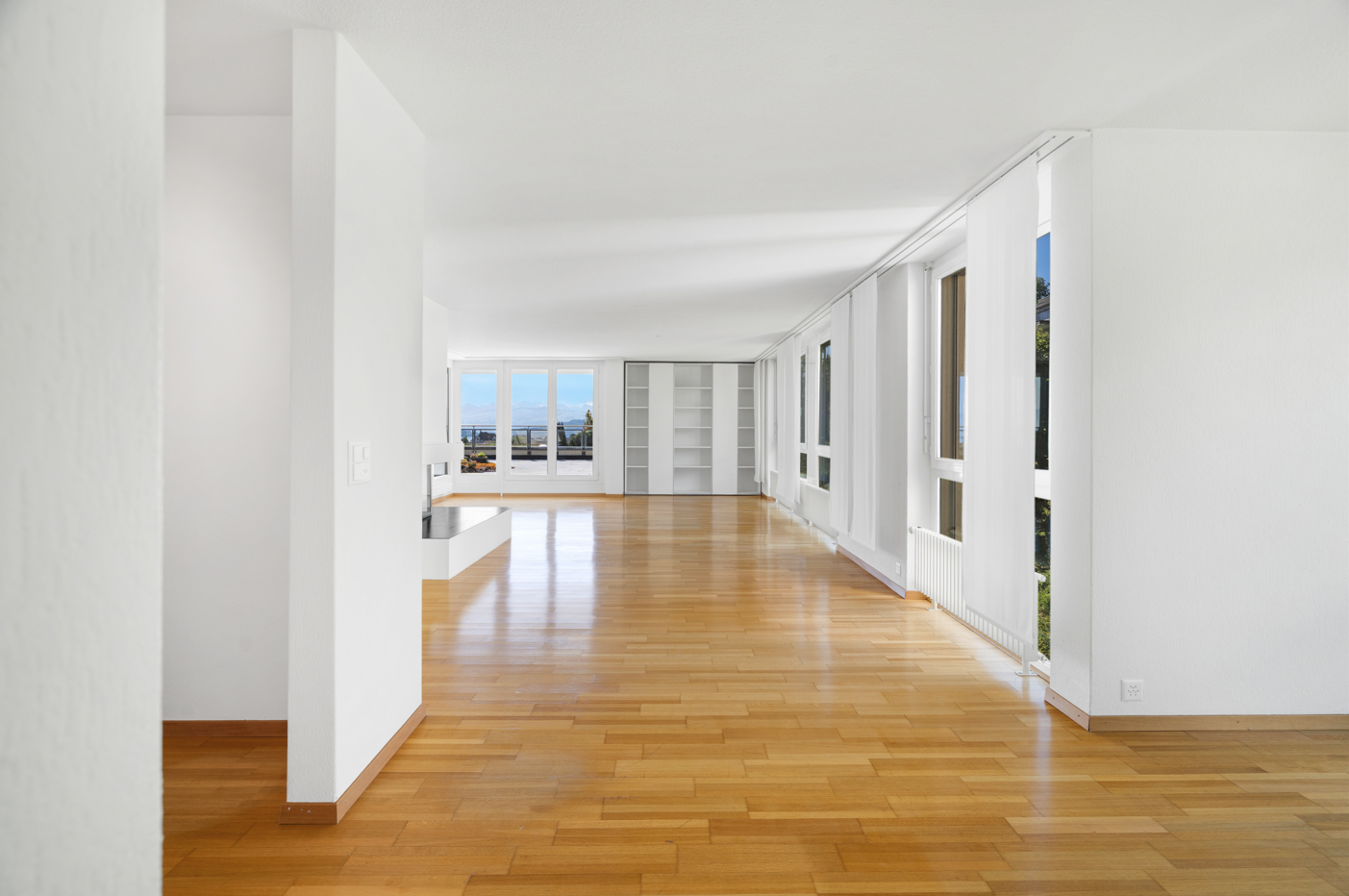 Heller, leerer Wohnbereich mit Parkettboden und großer Fensterfront