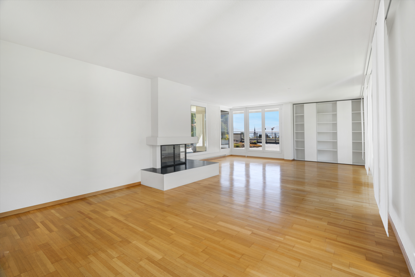 Großer leerer Wohnraum mit Kamin und Fensterfront