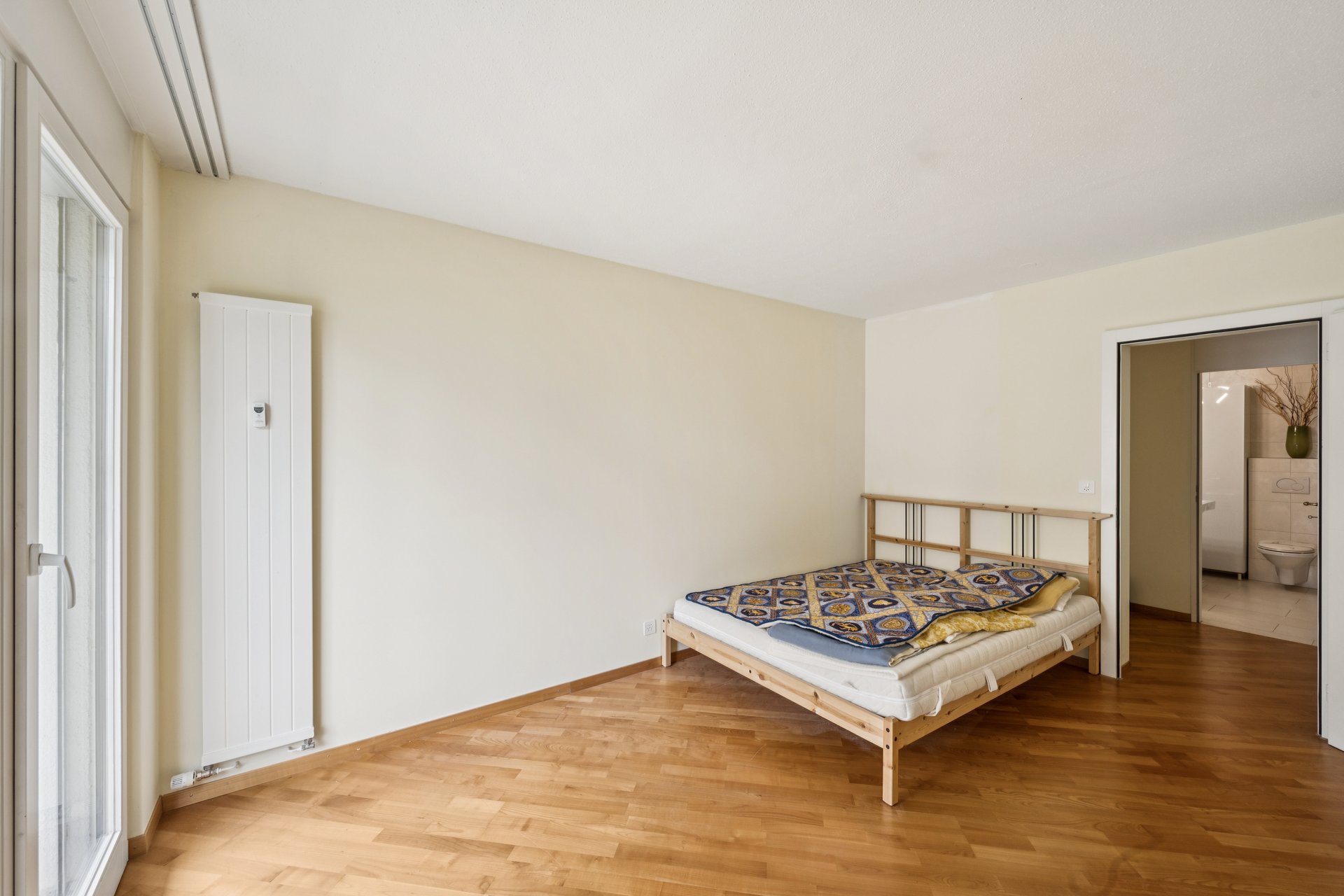 Helles Schlafzimmer mit einfachem Bett und Blick ins Bad