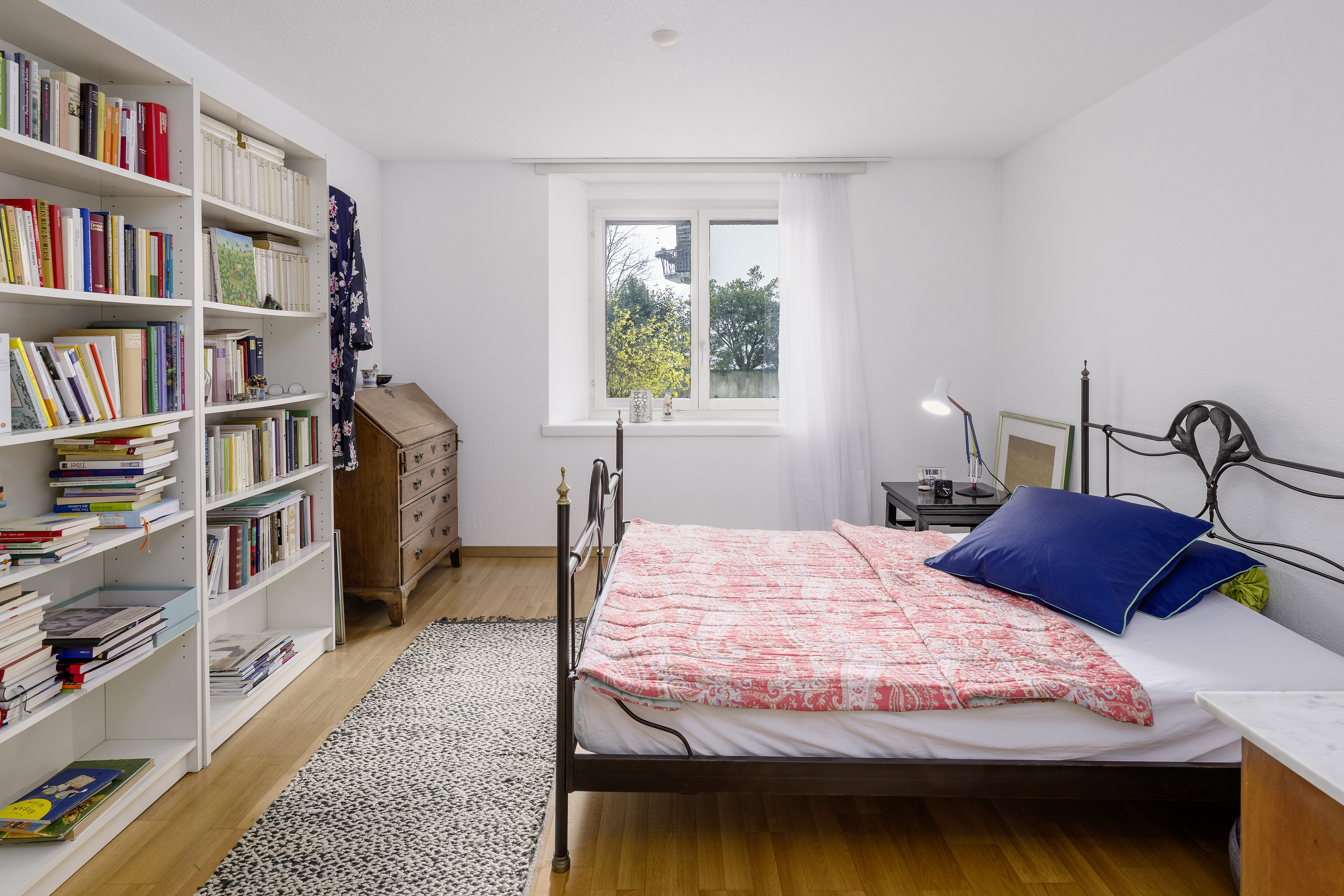Helles Schlafzimmer mit Bücherregal und Metallbett