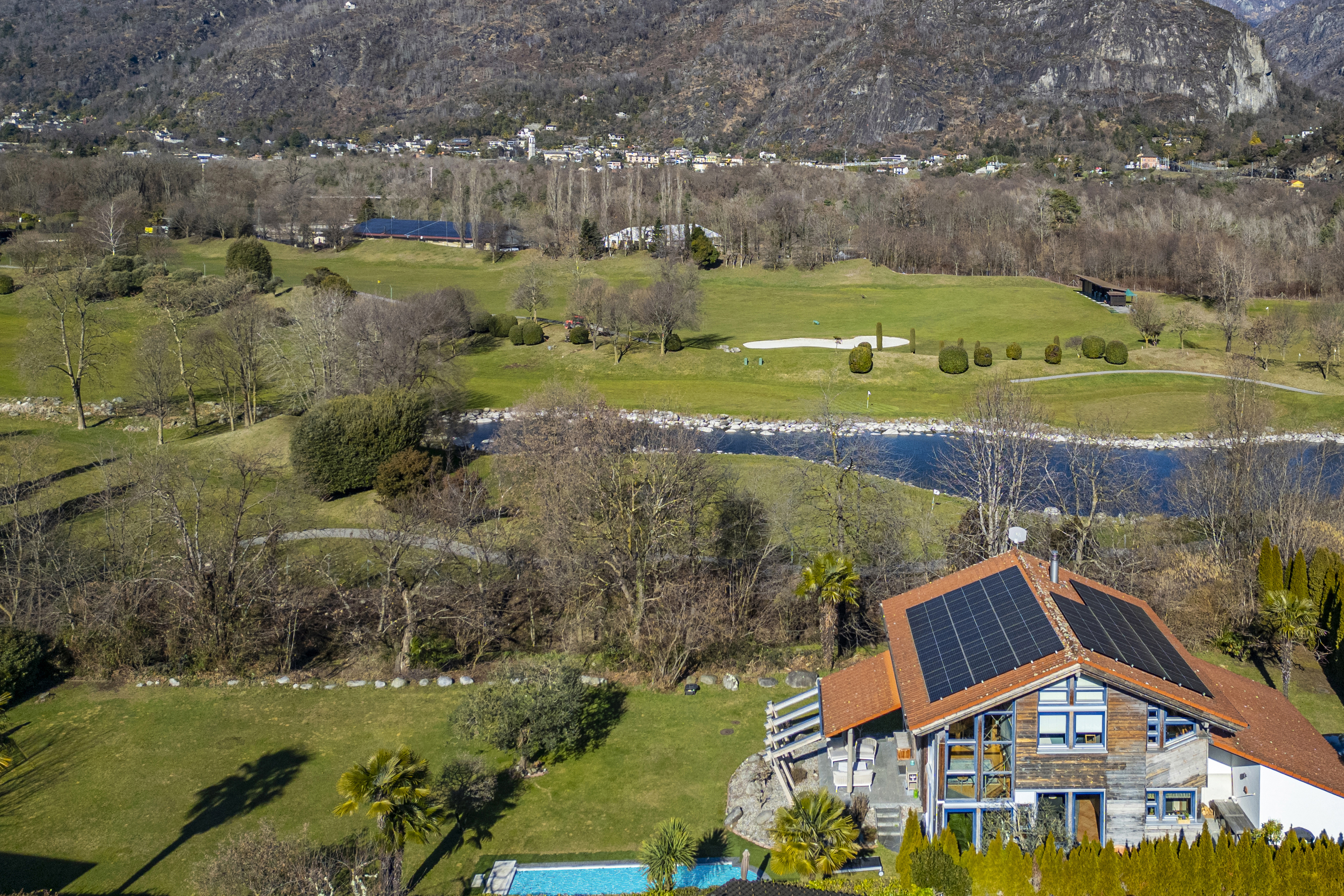 Luftaufnahme einer ländlichen Golf- und Wohnlandschaft mit Haus, Pool und Bergkulisse