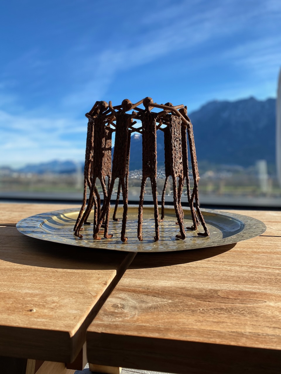 Dekorative Metallskulptur auf Holztisch mit Bergblick