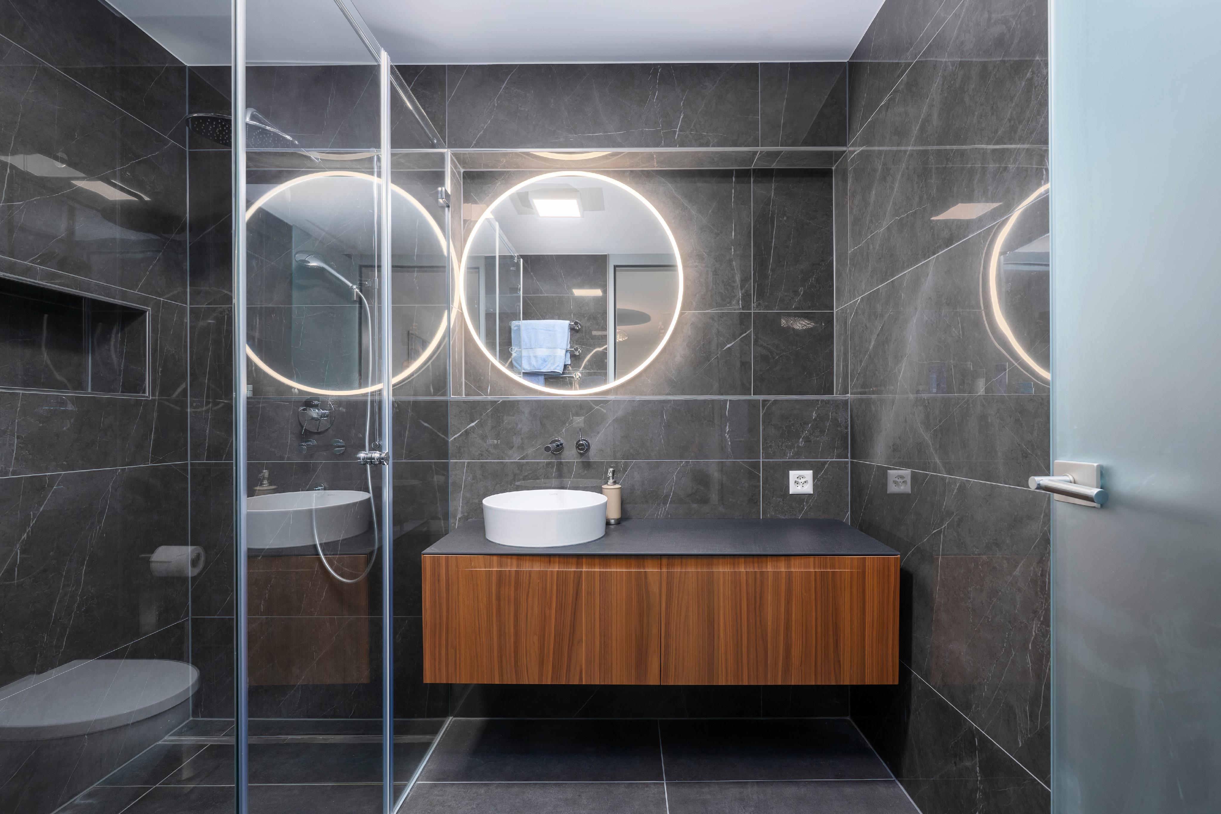 Modernes Badezimmer mit dunkler Steinoptik und LED-Spiegeln