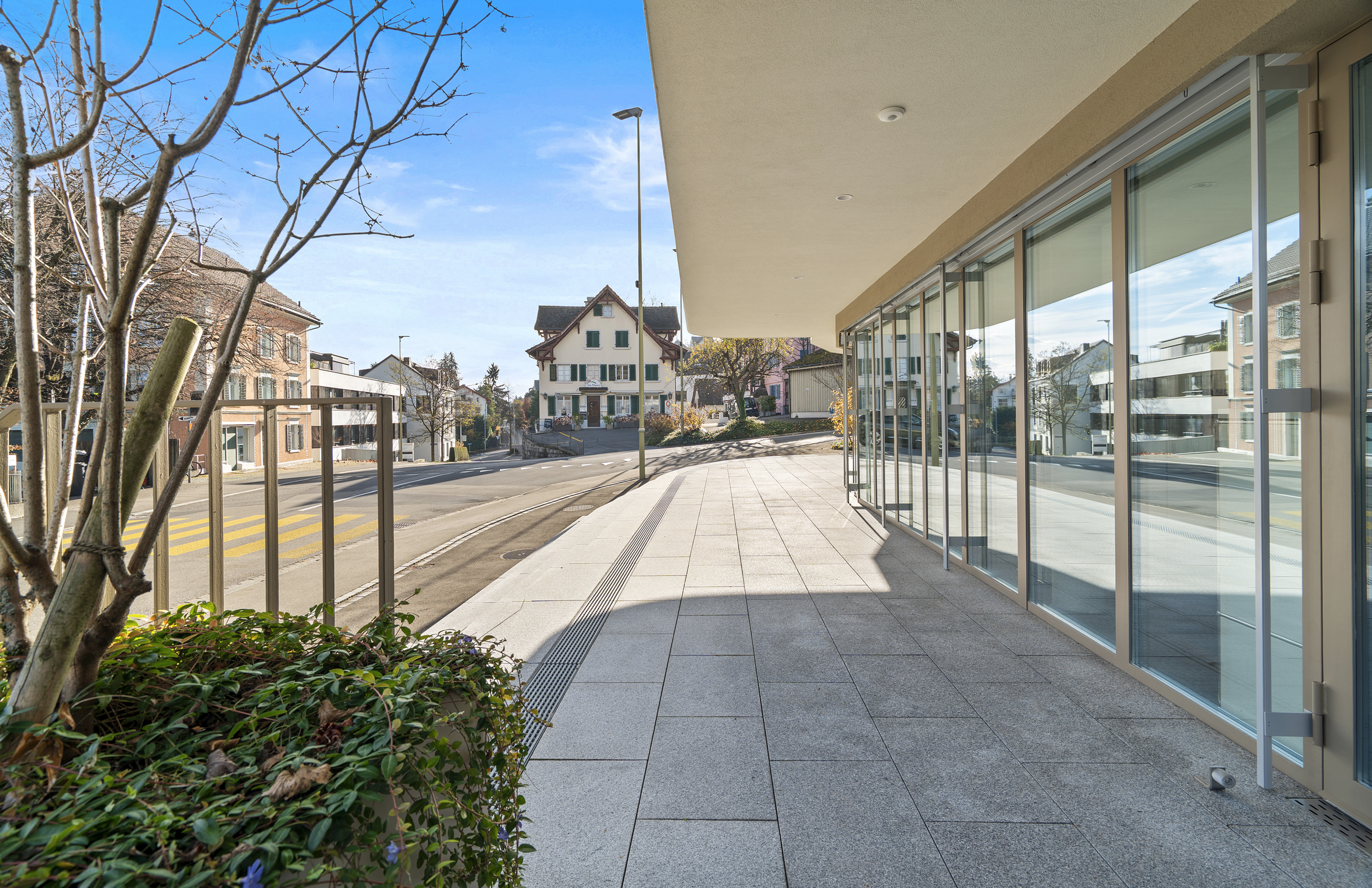 Überdachte Außenanlage mit Glasfassade an einer ruhigen Straße