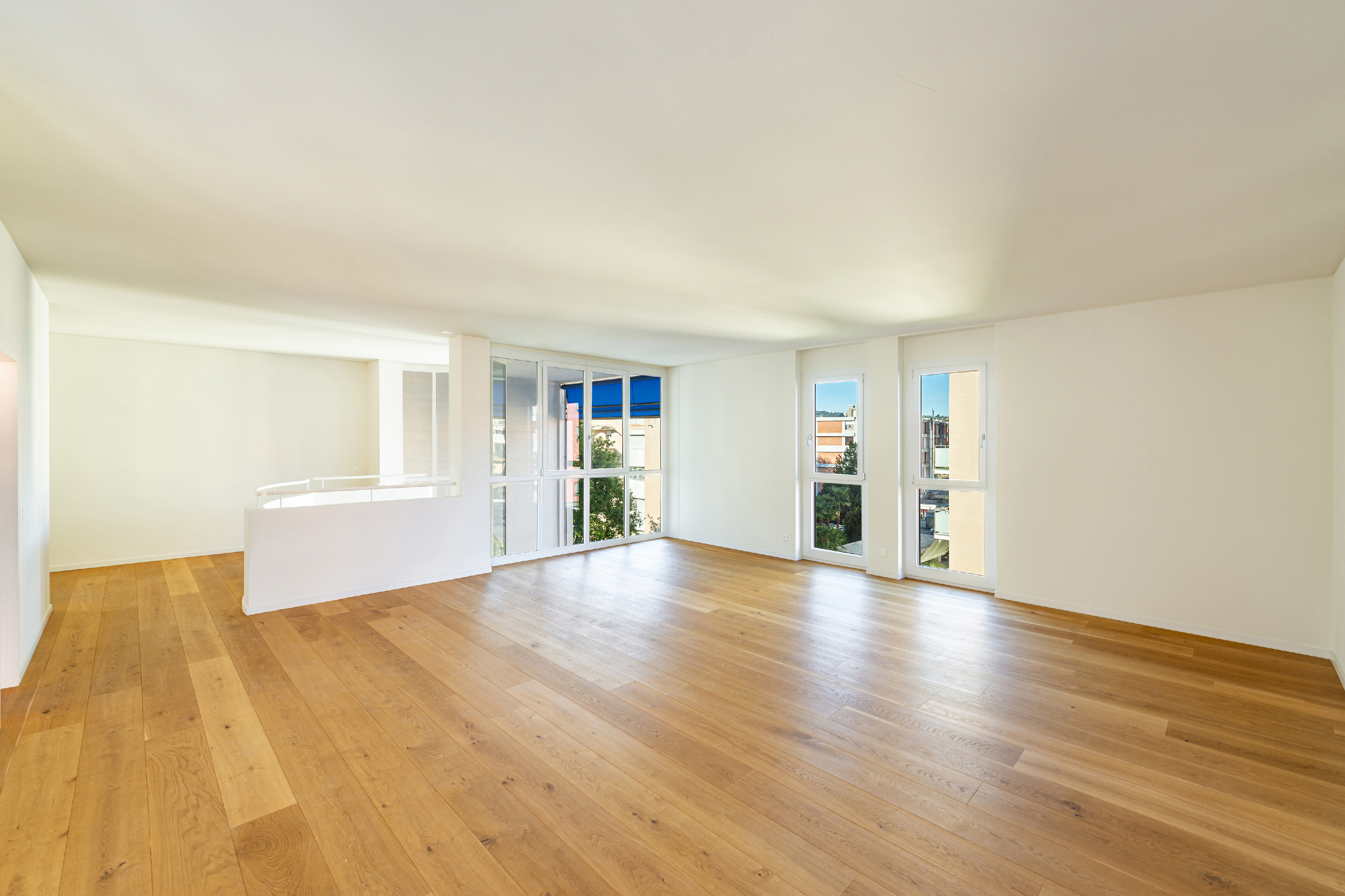 Heller leerer Wohnraum mit Holzboden und großen Fenstern