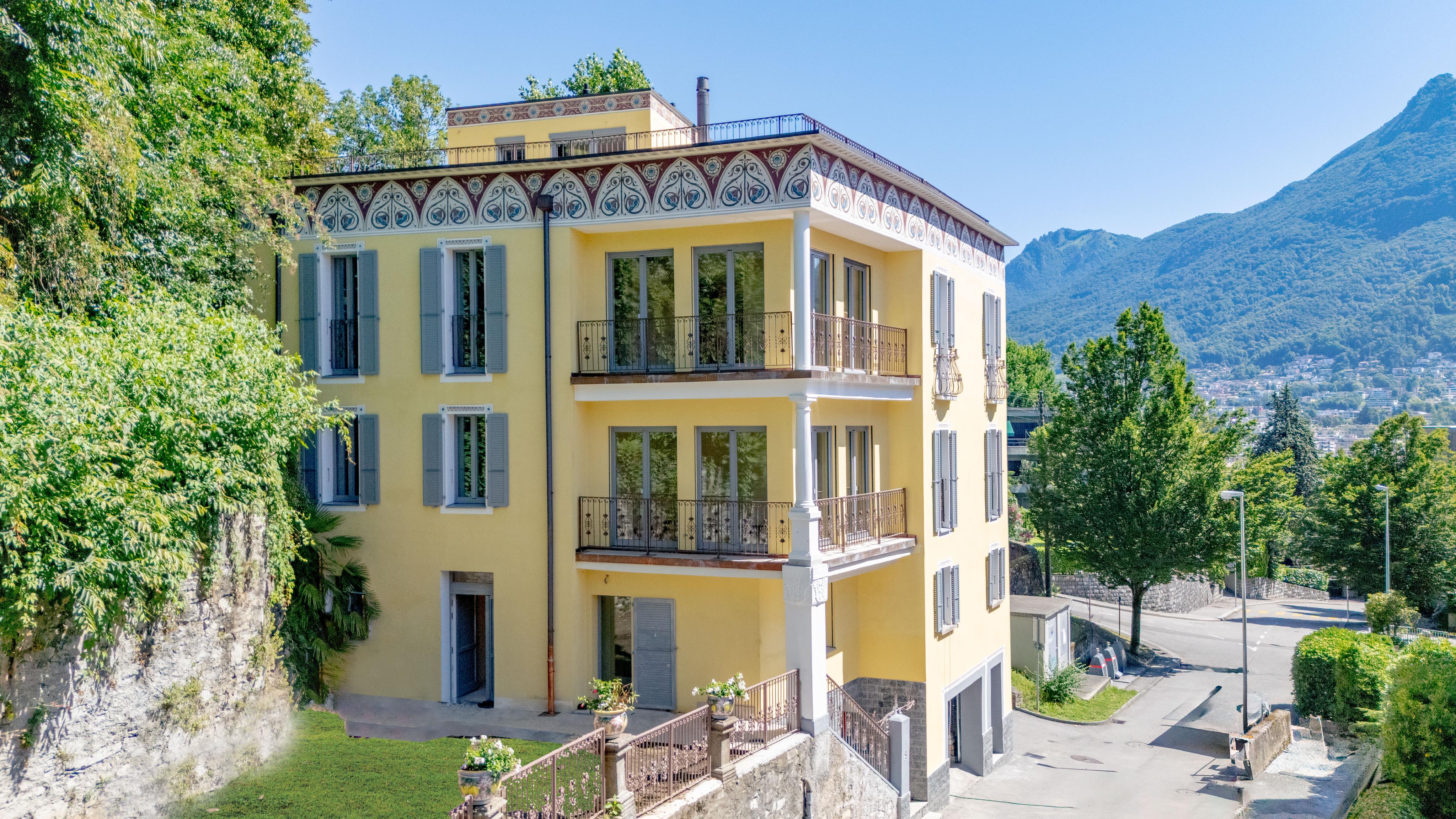 Außenansicht einer gelben Villa mit Balkon und Bergblick