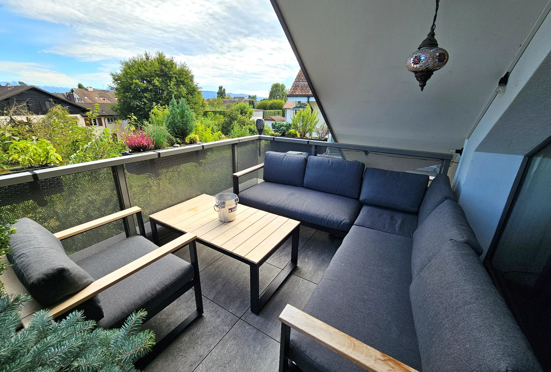 Überdachter Balkon mit Lounge-Möbeln und Gartenblick
