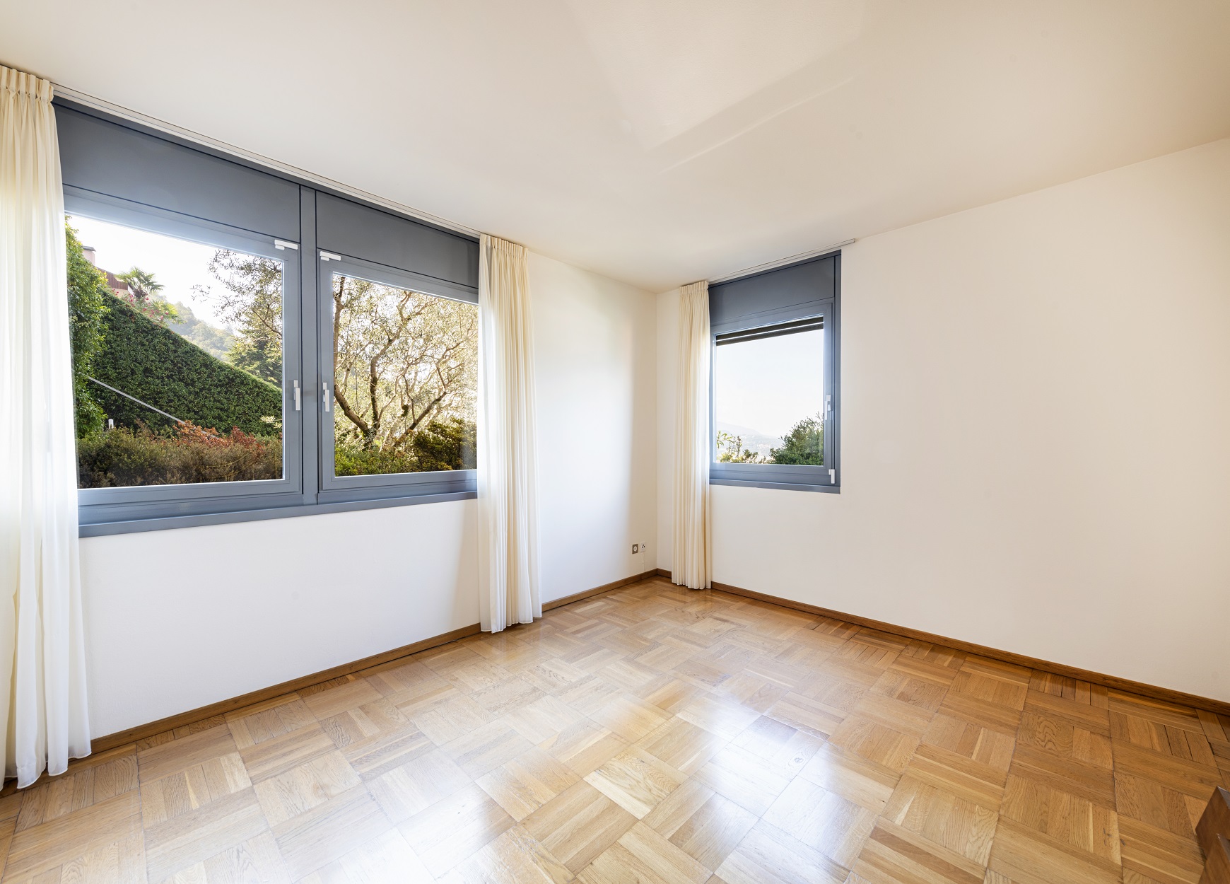 Helles, leeres Zimmer mit großen Fenstern und Holzparkett