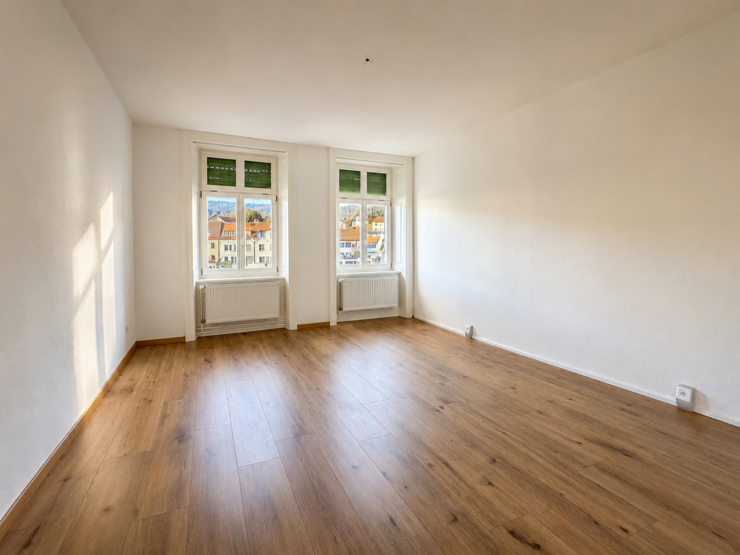 Heller leerer Raum mit Holzfußboden und zwei Fenstern