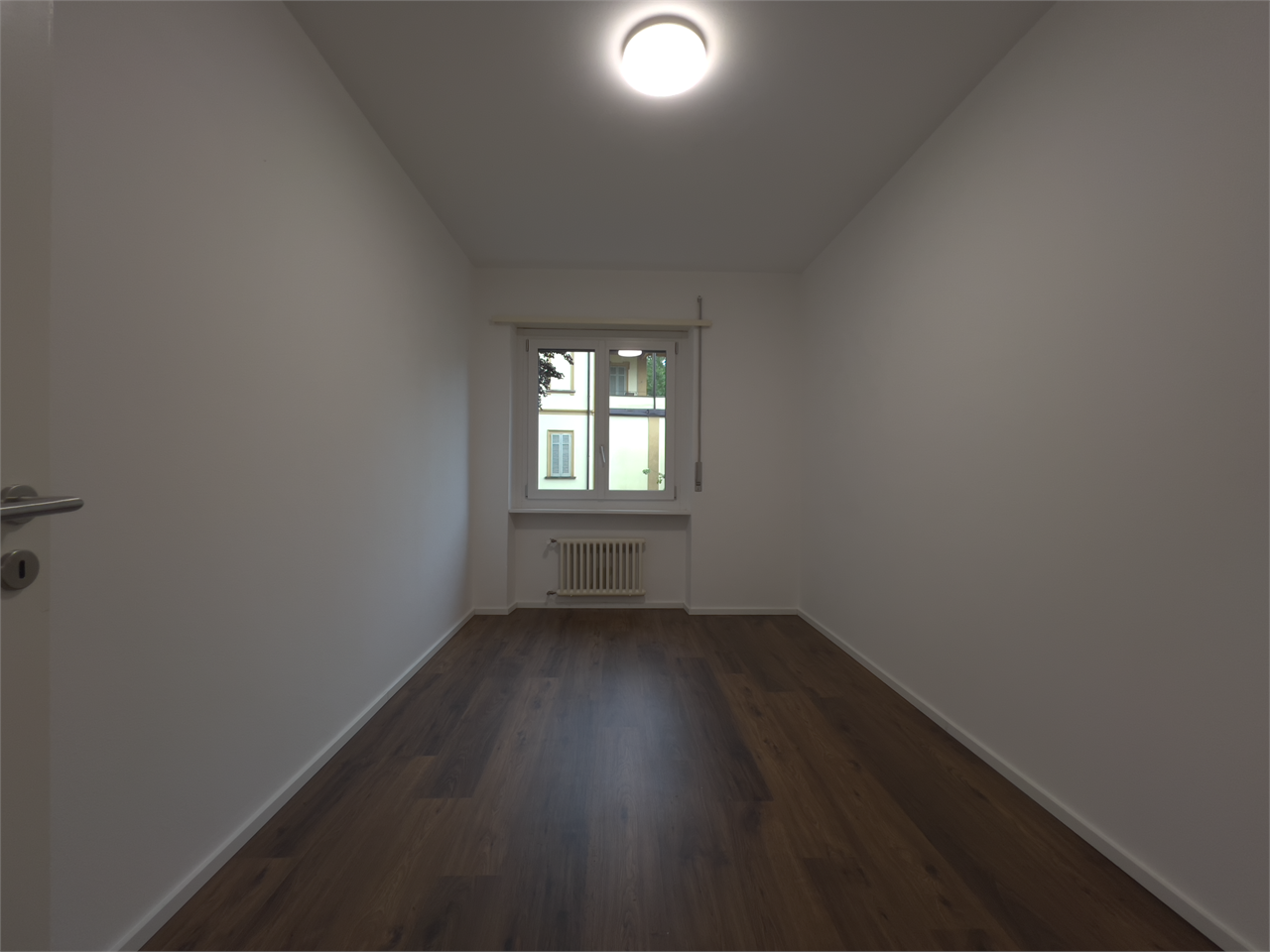 Schmaler, leerer Raum mit Fenster und Heizkörper