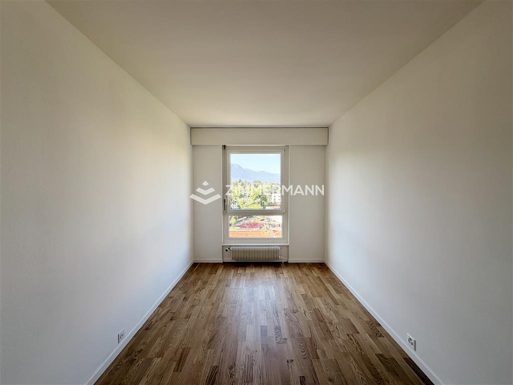 Schmales, leeres Zimmer mit Fenster und Holzparkett