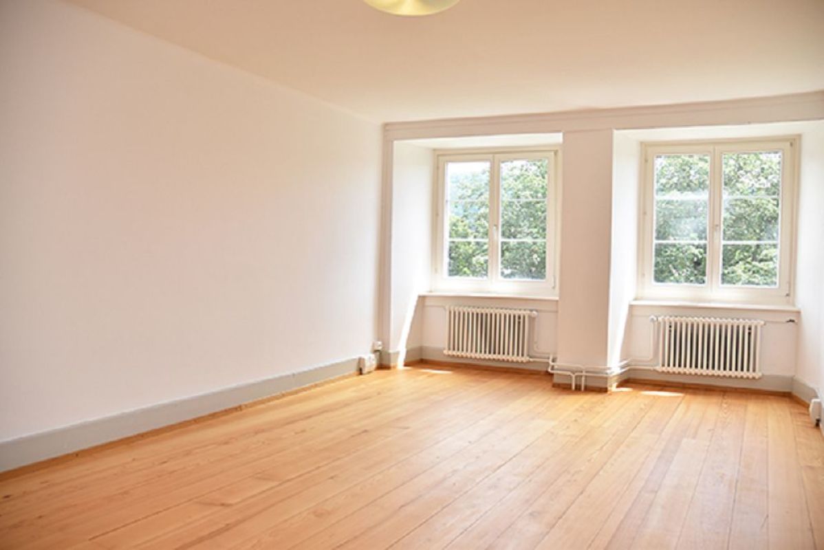 Heller leerer Wohnraum mit Dielenboden und zwei Fenstern