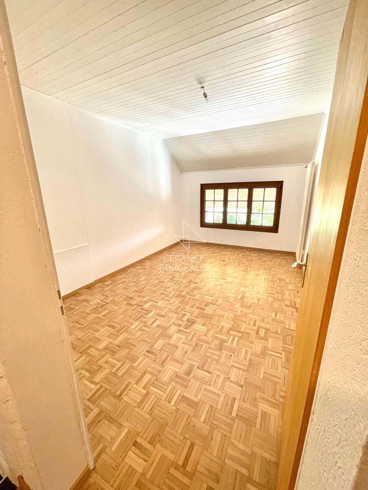 Leerer, heller Raum mit Parkettboden und Holzfenster
