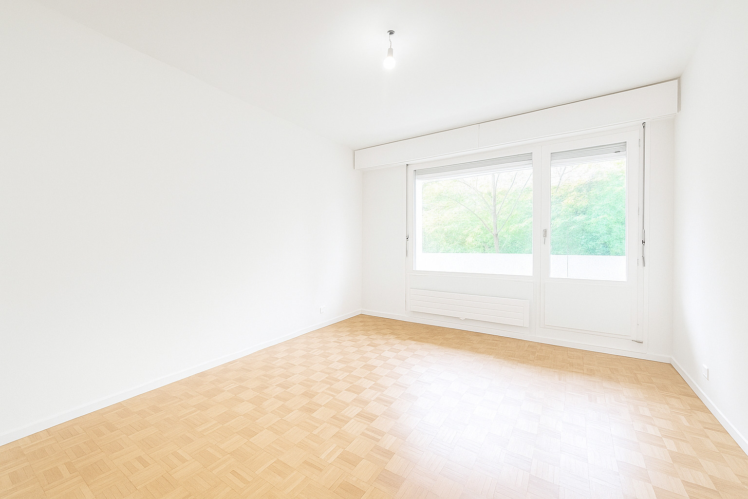 Leerer heller Raum mit Parkettboden und großem Fenster