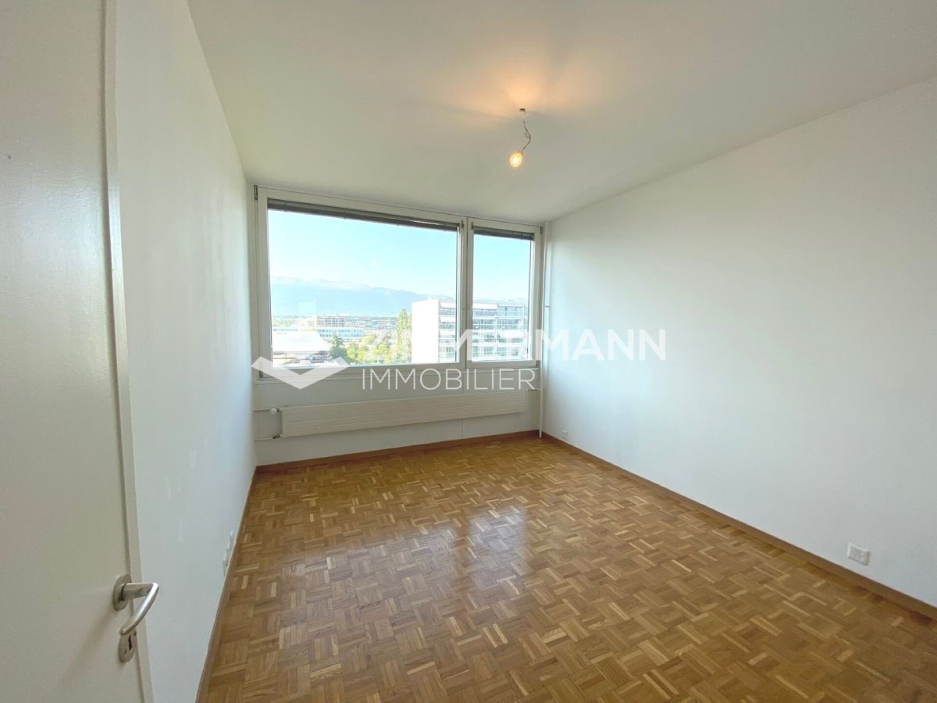 Leerer heller Raum mit Parkettboden und großem Fenster