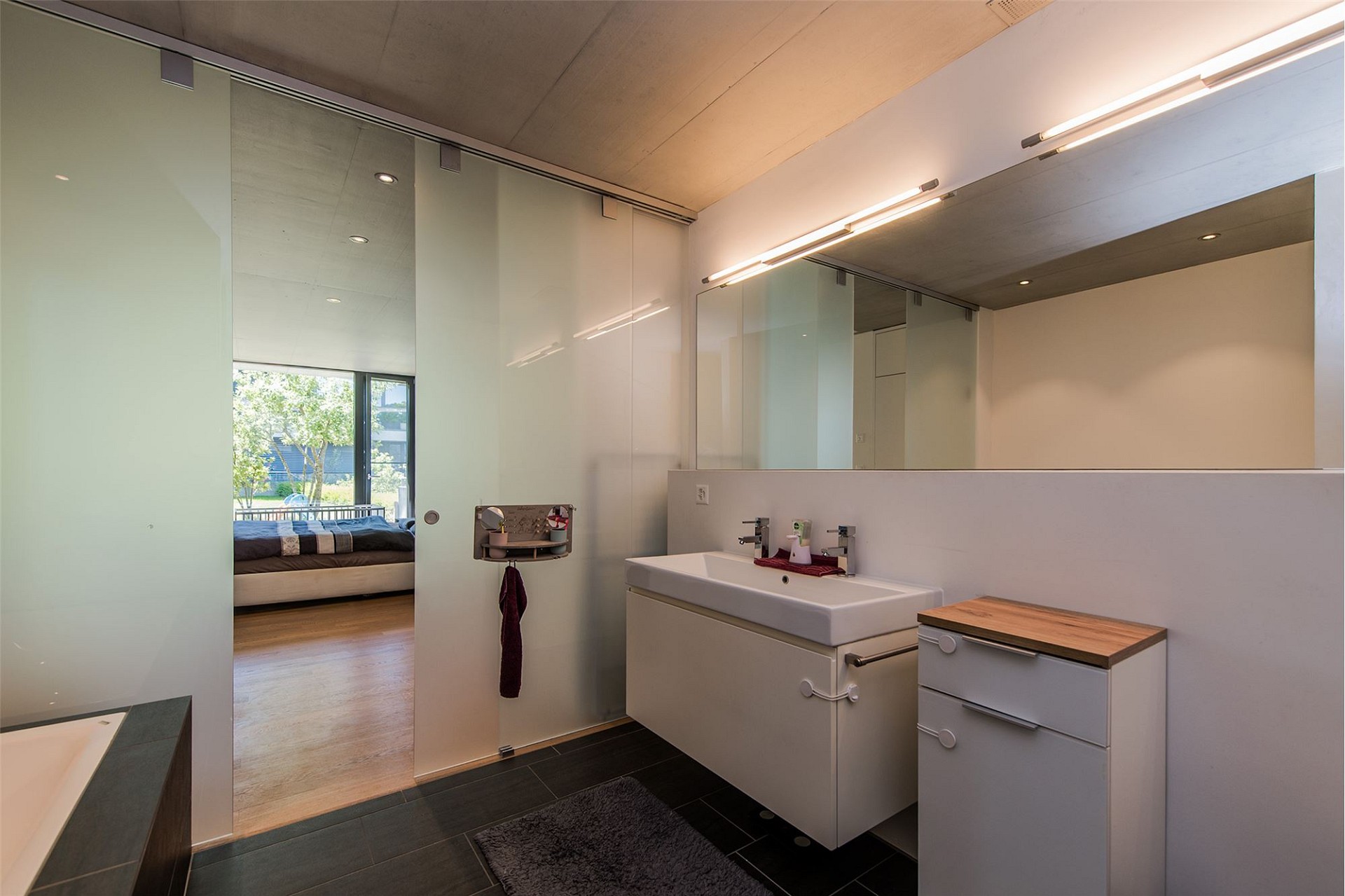 Modernes Badezimmer mit Glas-Schiebetür und Blick ins Schlafzimmer