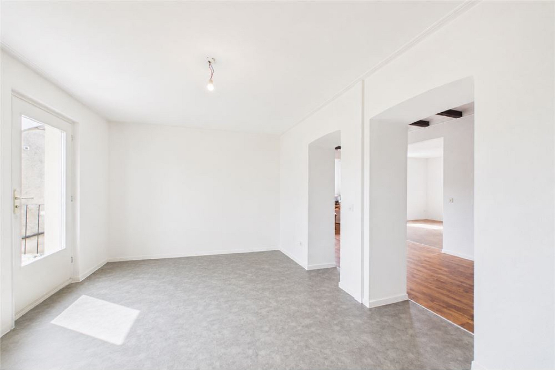 Helles, leerstehendes Zimmer mit weißen Wänden und grauem Bodenbelag