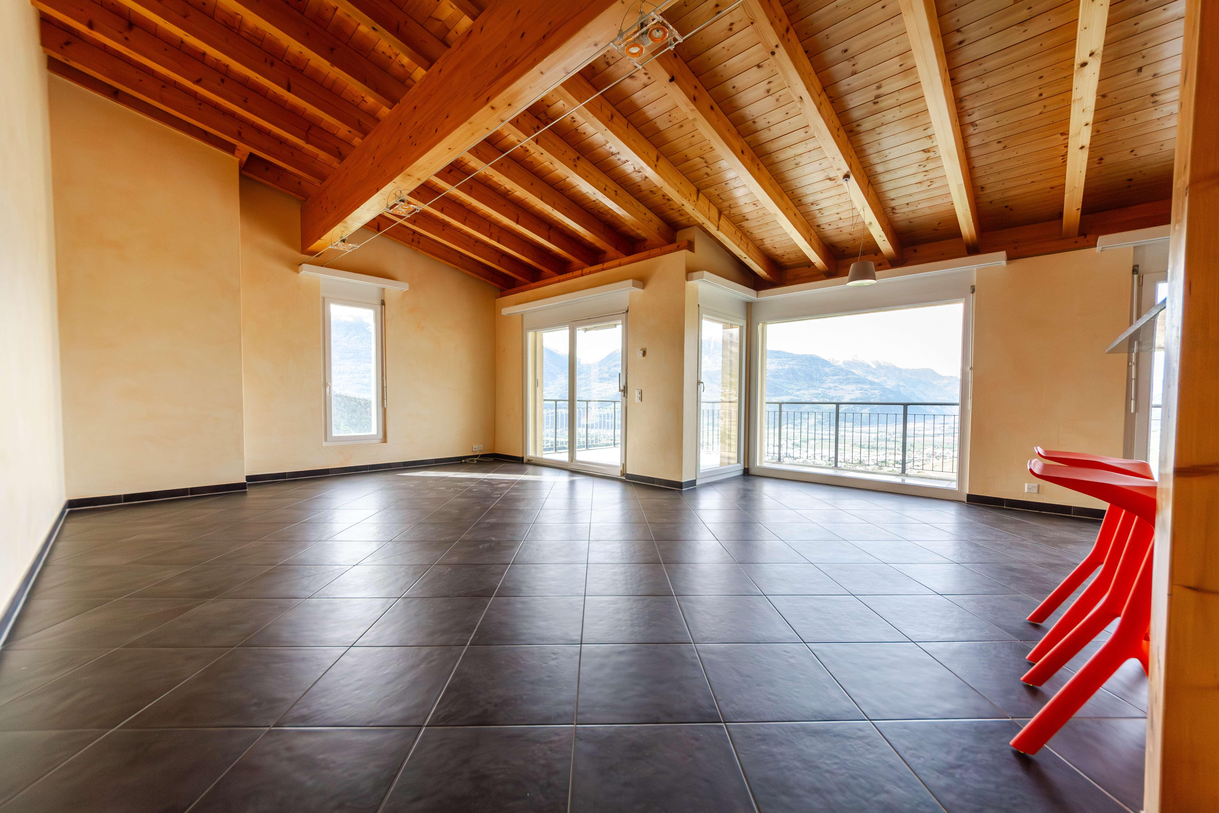 Großer leerer Wohnraum mit Holzbalkendecke und Panoramafenstern