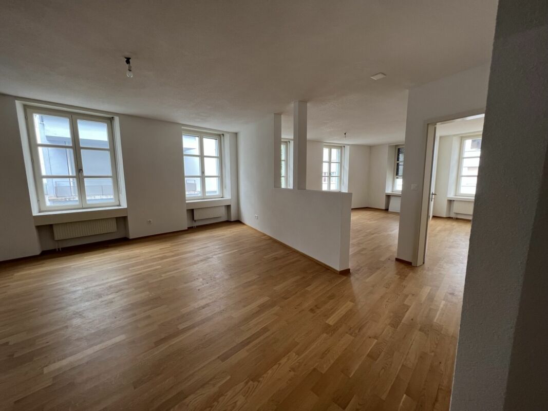 Heller, leerer Wohnraum mit Parkett und mehreren Fenstern