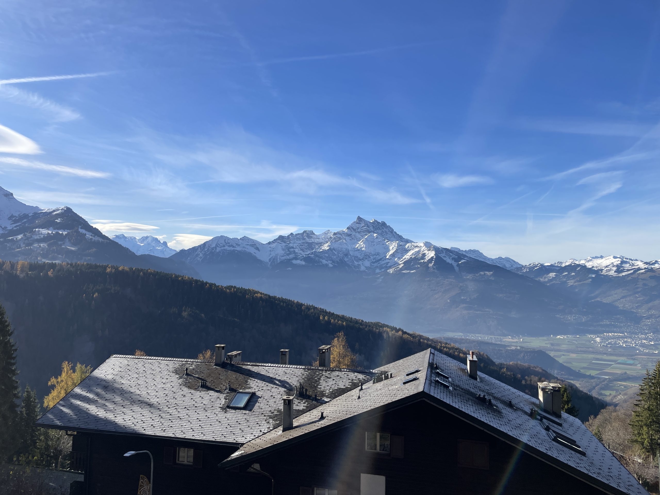 Alpenpanorama mit schneebedeckten Bergen über einem dunklen Chalet-Dach