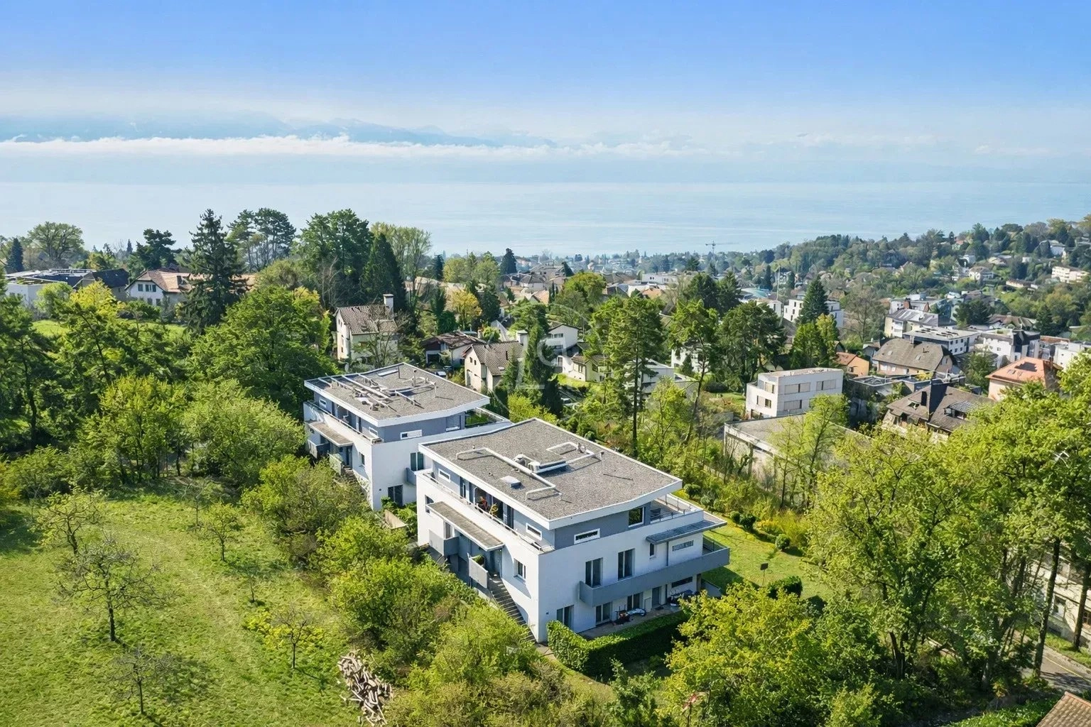 Luftaufnahme von zwei modernen Wohnhäusern in grüner Hanglage mit Seeblick.