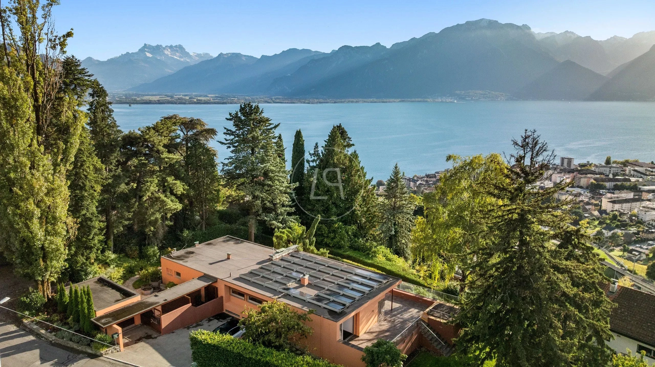 Seeblick über ein Haus mit Flachdach und Alpenpanorama