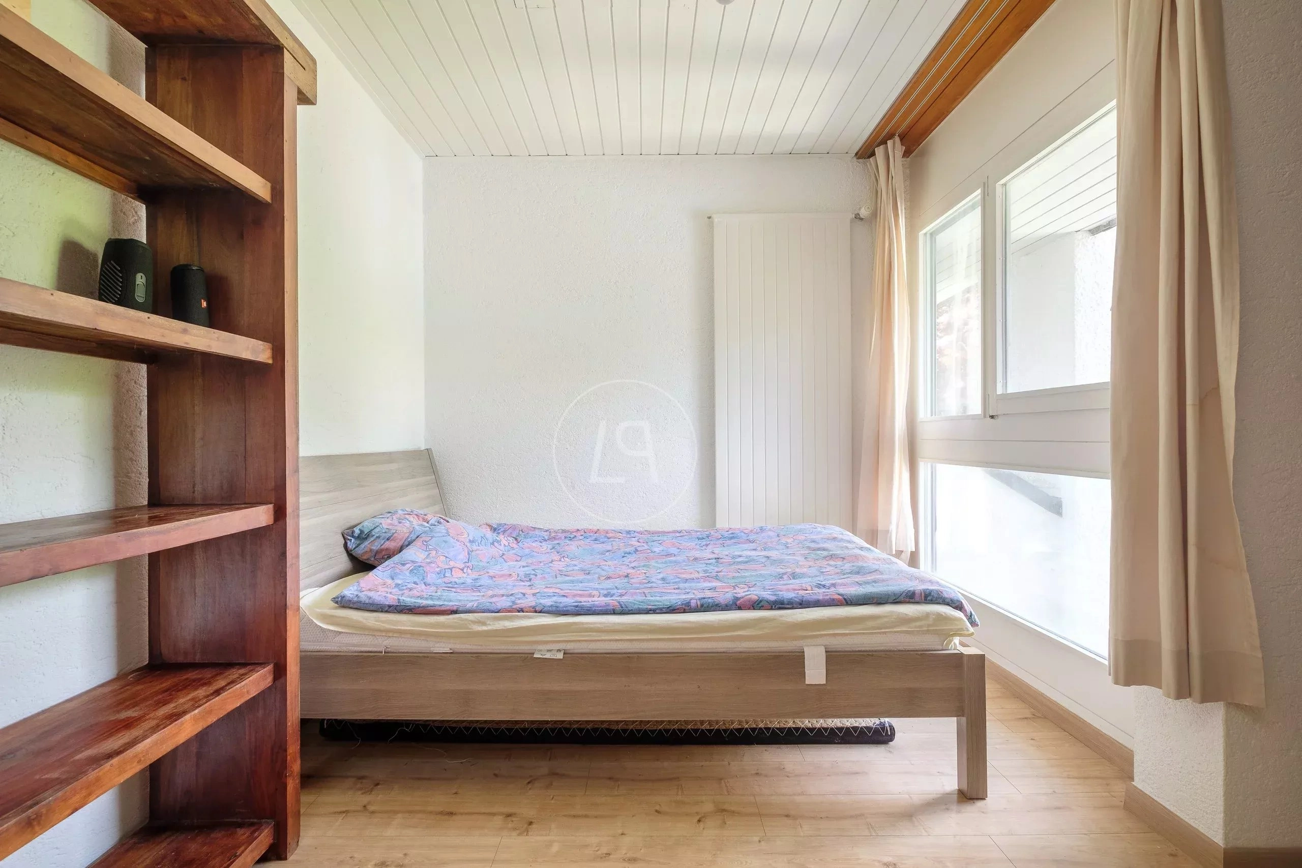Helles Schlafzimmer mit Holzregal und großem Fenster
