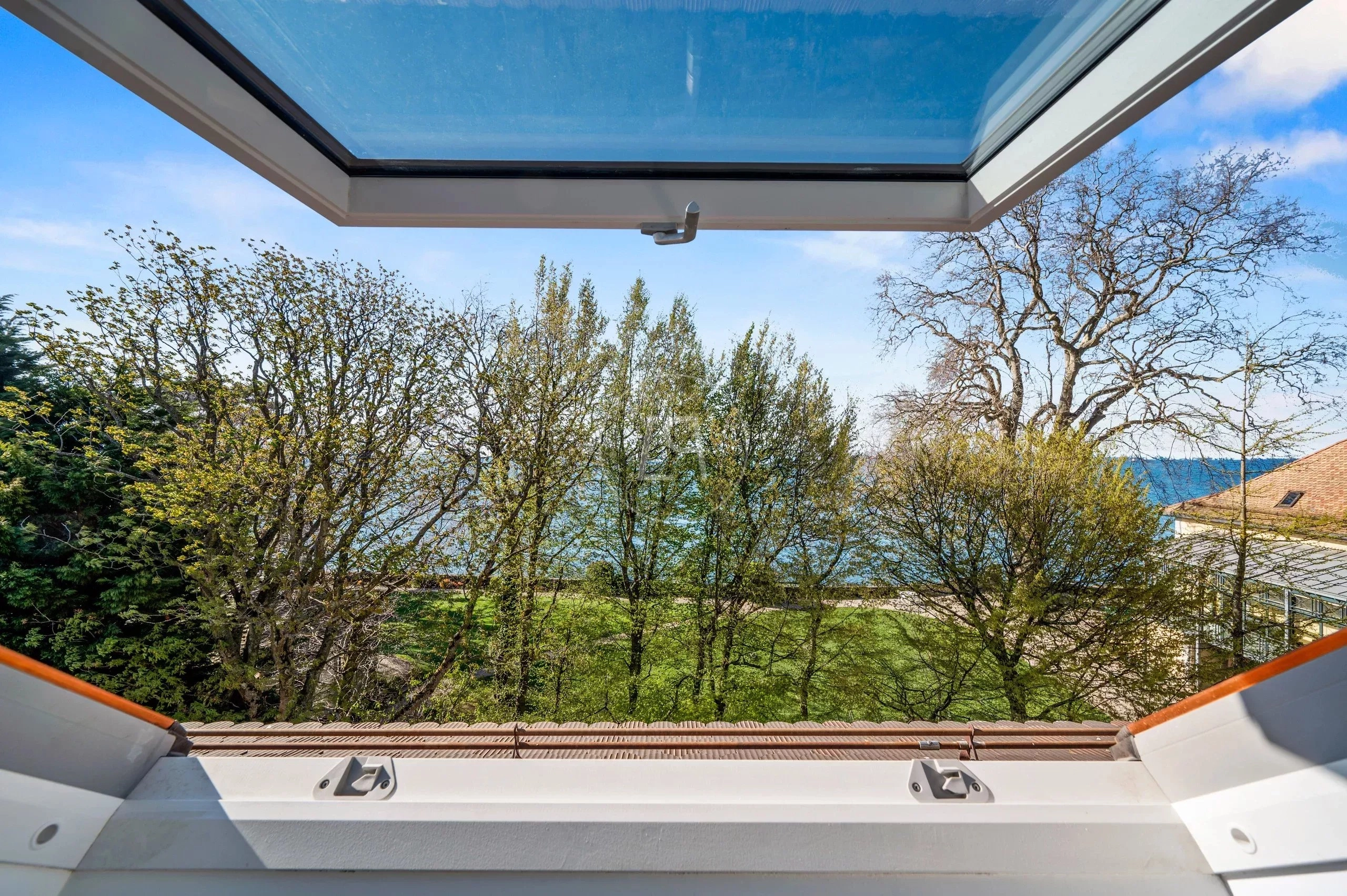 Blick durch ein Dachfenster auf Meer und Grünanlage