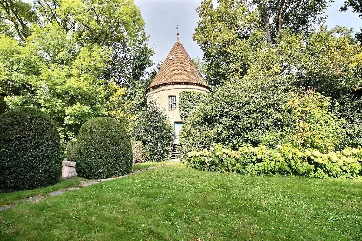 Runder Turm mit Spitzdach in parkähnlichem Garten
