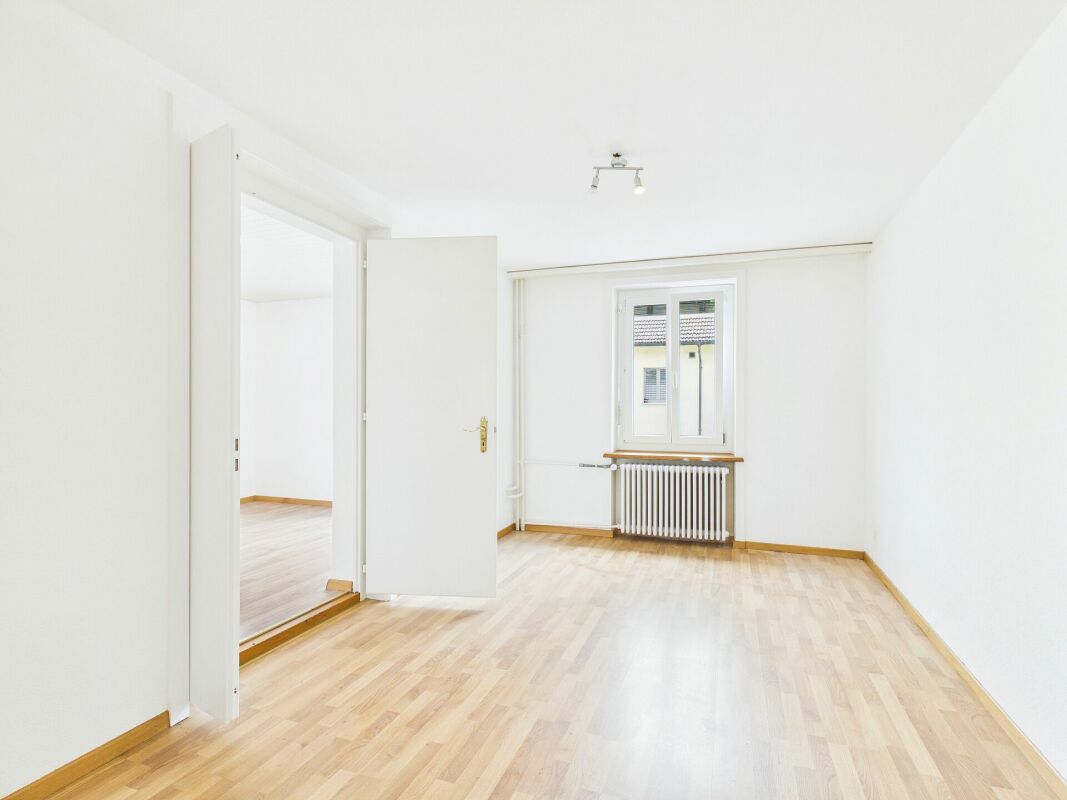 Helles, leeres Zimmer mit Holzboden und Fenster