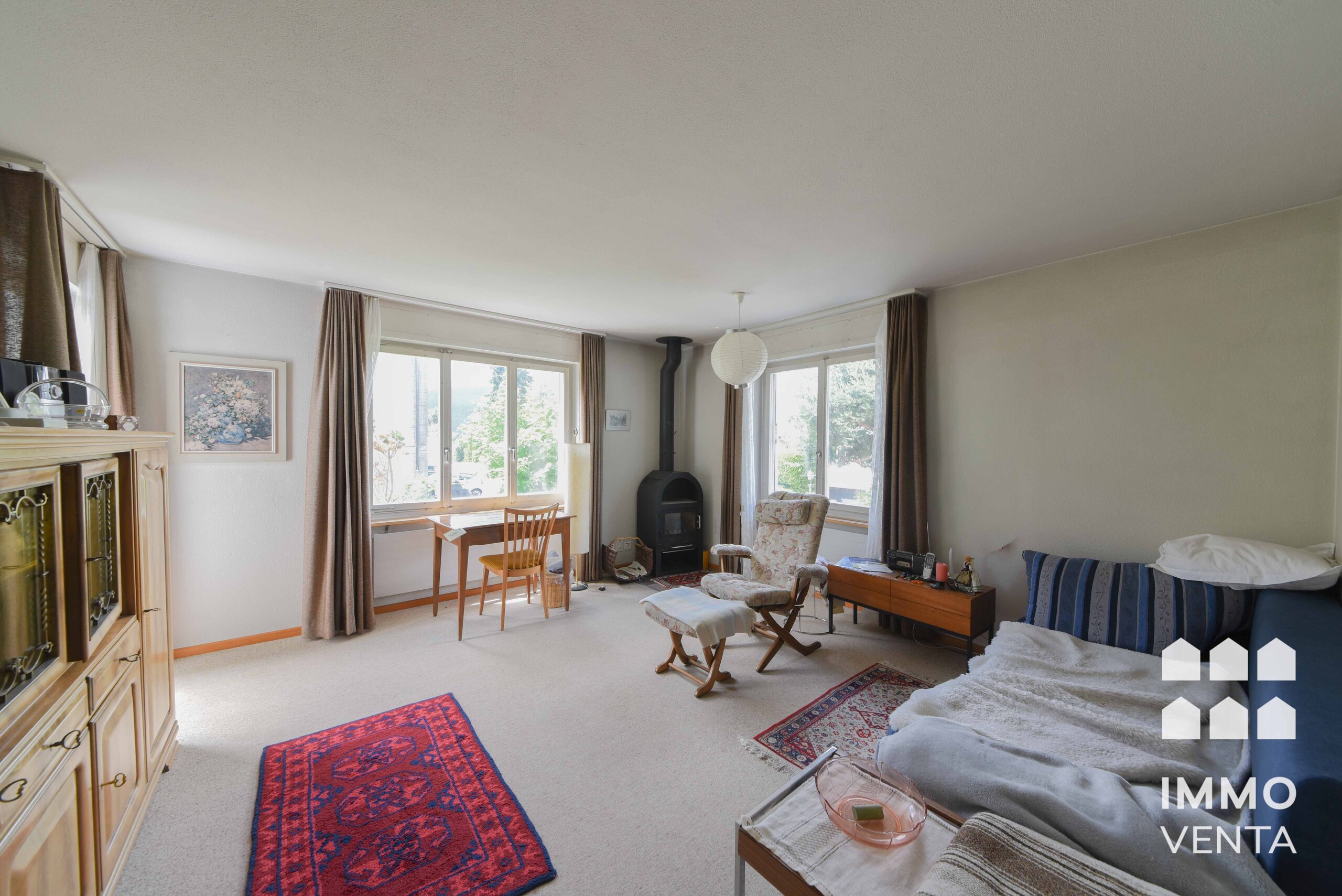 Gemütliches Wohnzimmer mit großen Fenstern und Kaminofen