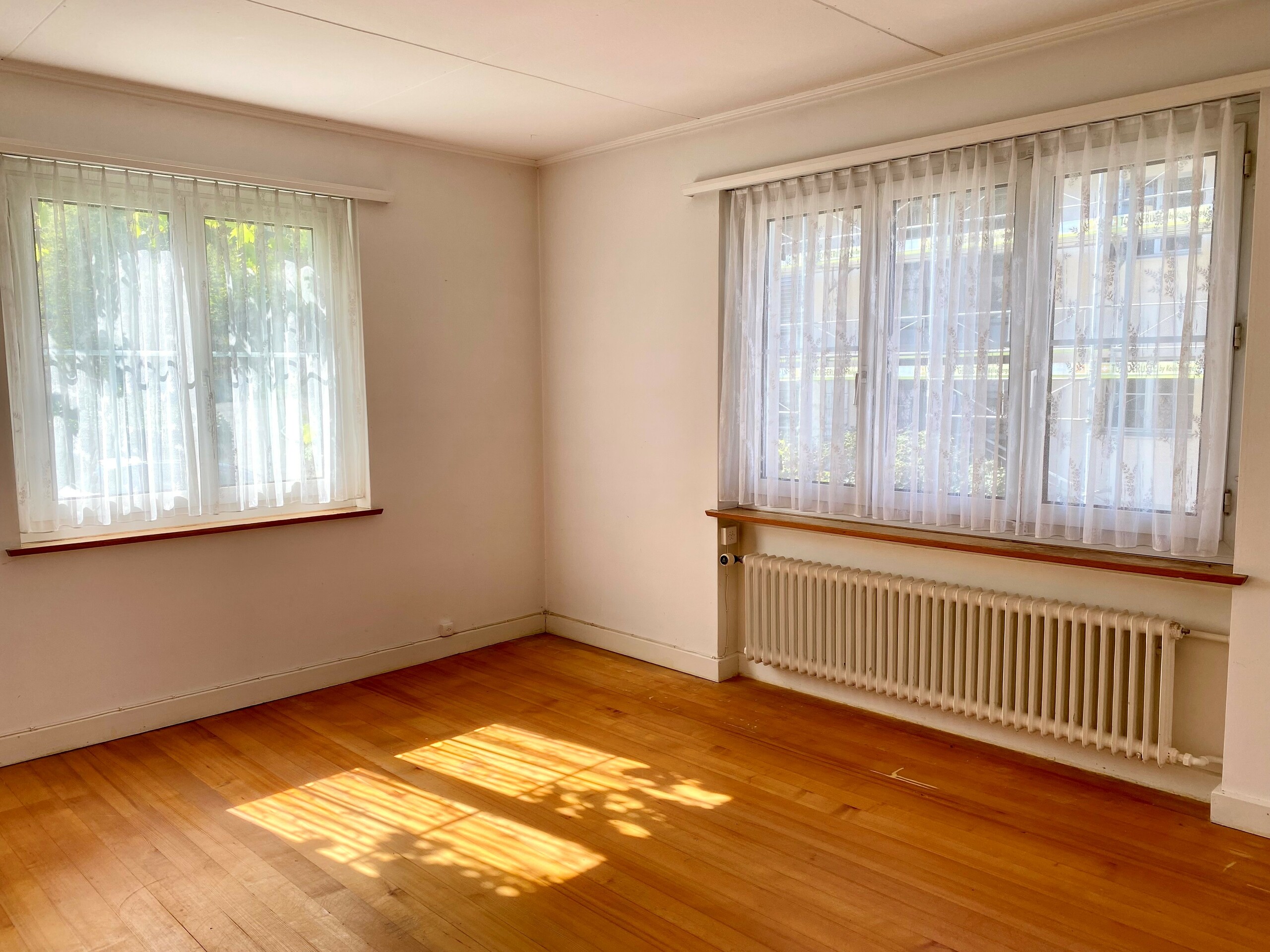 Heller leerer Wohnraum mit Parkettboden und zwei Fenstern