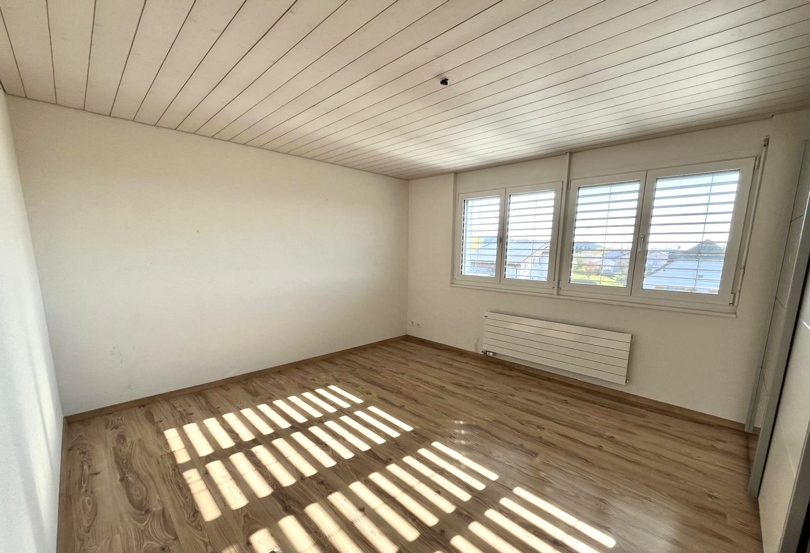 Heller leerer Raum mit Holzoptik-Boden und Fensterfront