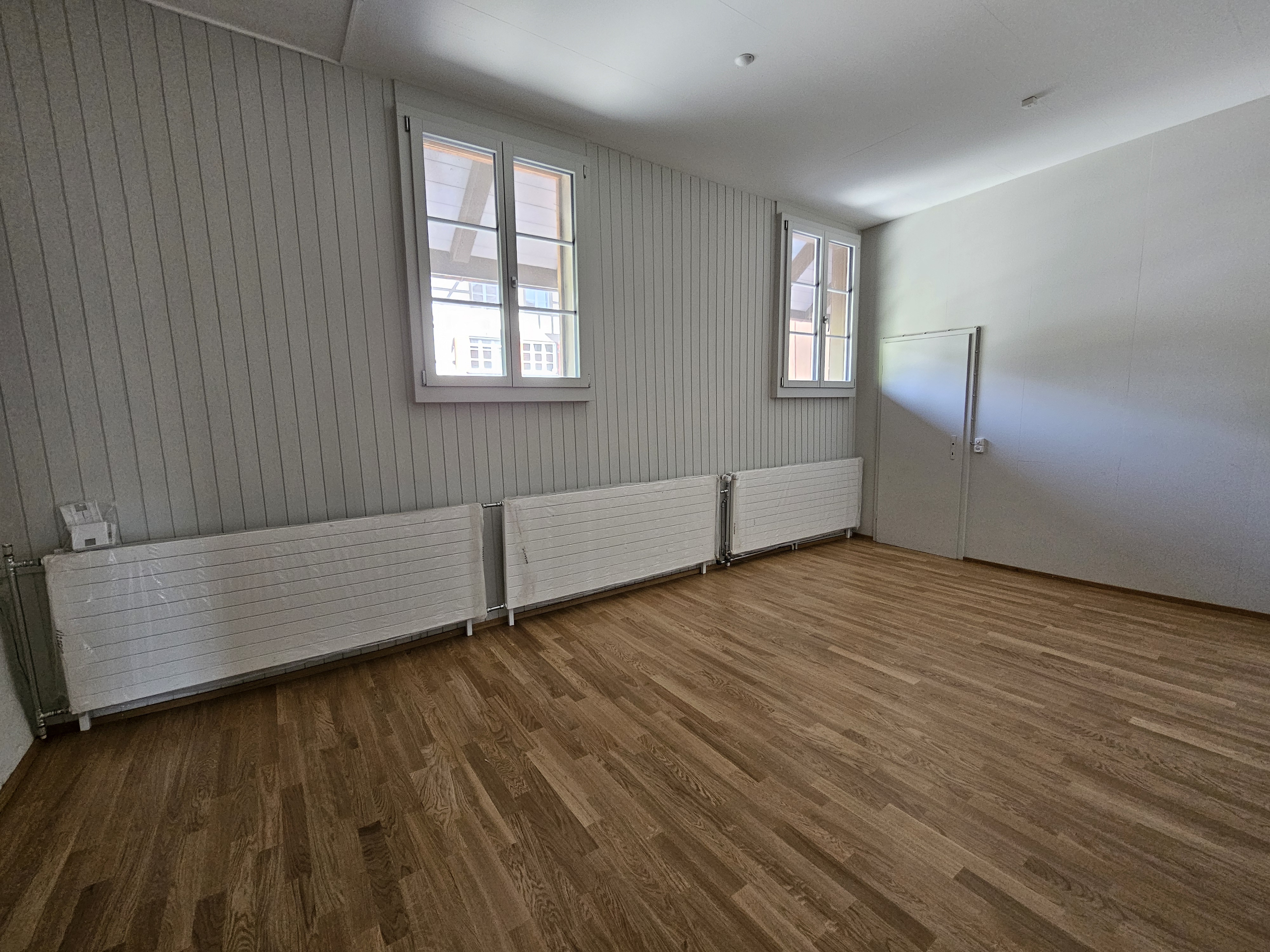 Heller leerer Raum mit Holzoptikboden und hohen Fenstern