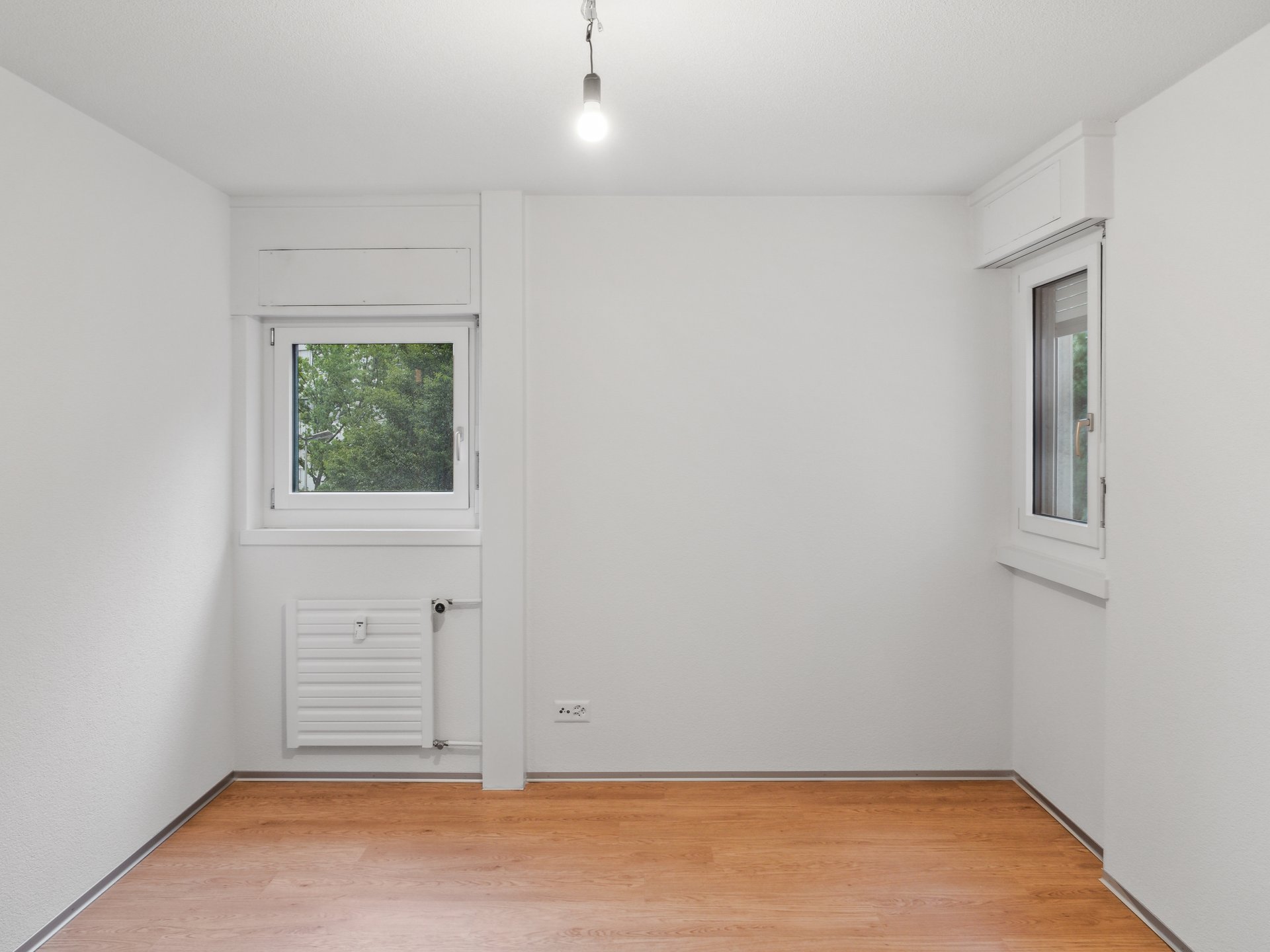 Leerer, renovierter Raum mit zwei Fenstern und Holzoptikboden