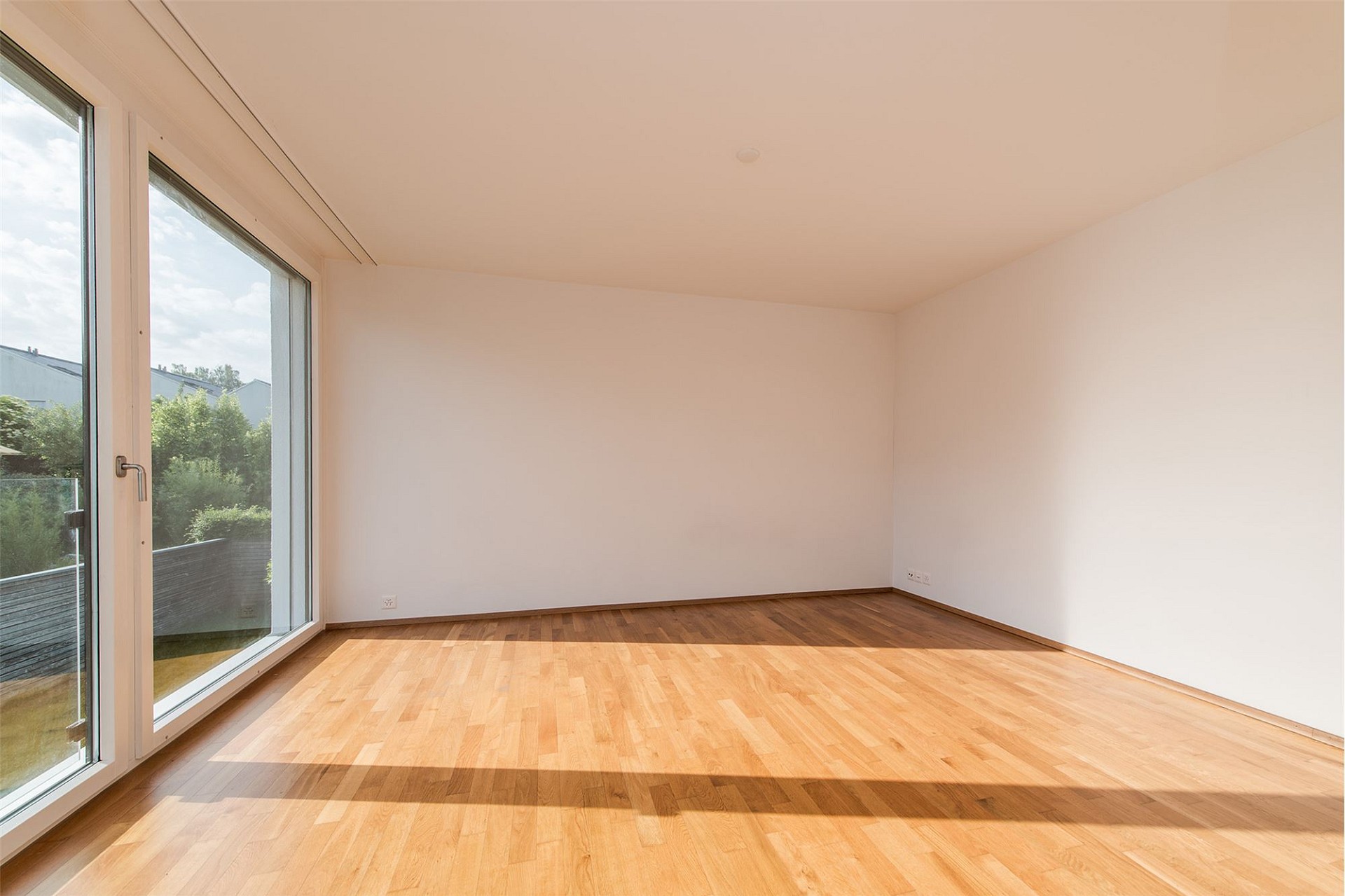 Helles, leeres Zimmer mit Holzboden und großem Fenster