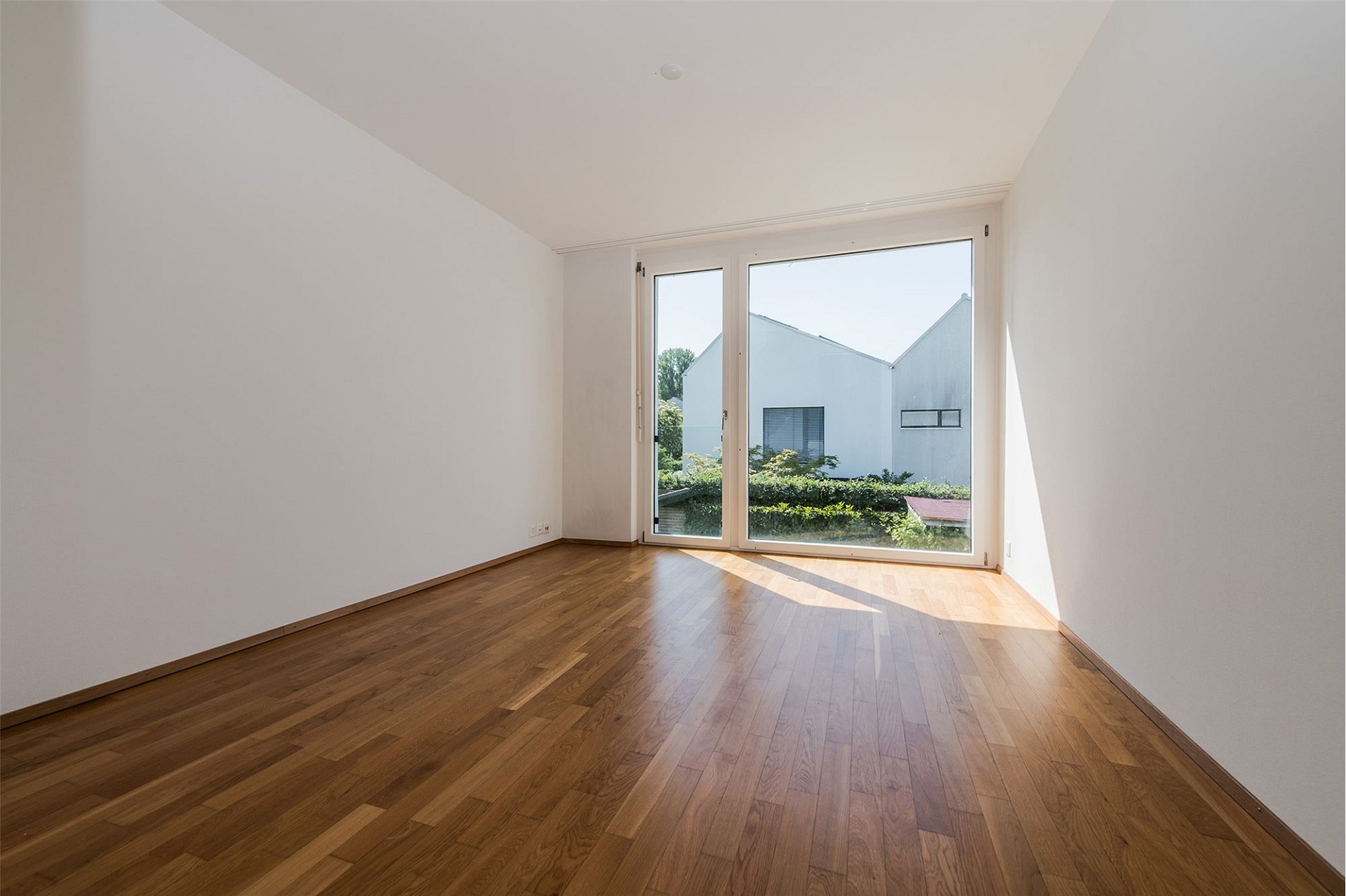 Heller leerer Raum mit Parkett und großem Fenster
