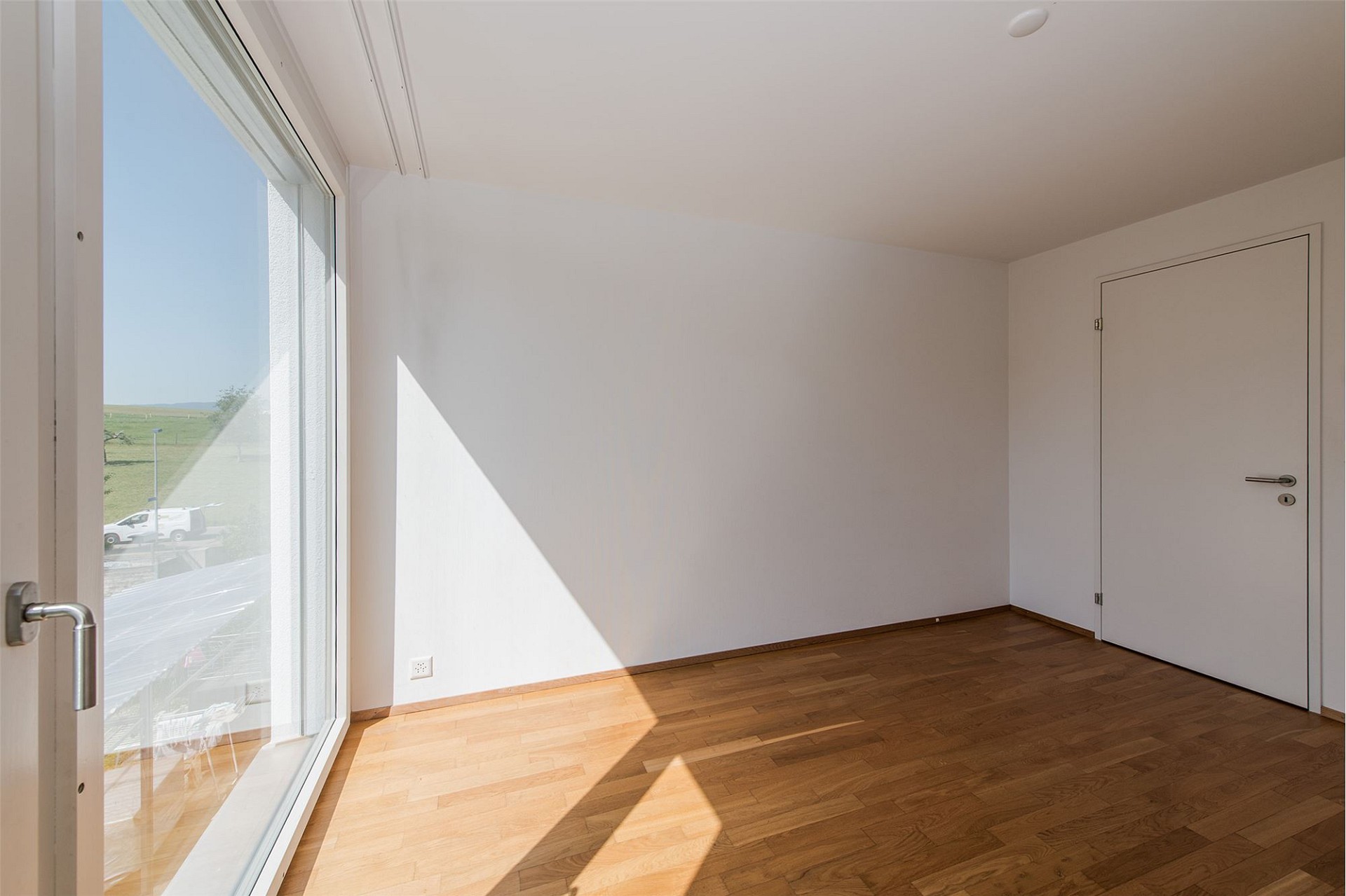 Helles, leeres Zimmer mit großem Fenster und Holzboden