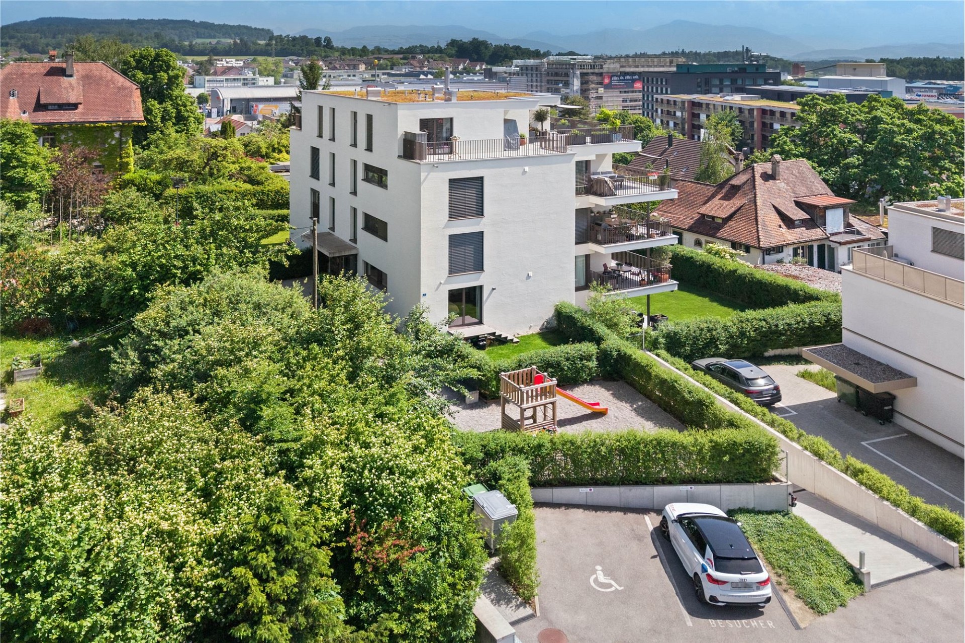 Luftaufnahme eines modernen Mehrfamilienhauses mit Garten und Spielbereich