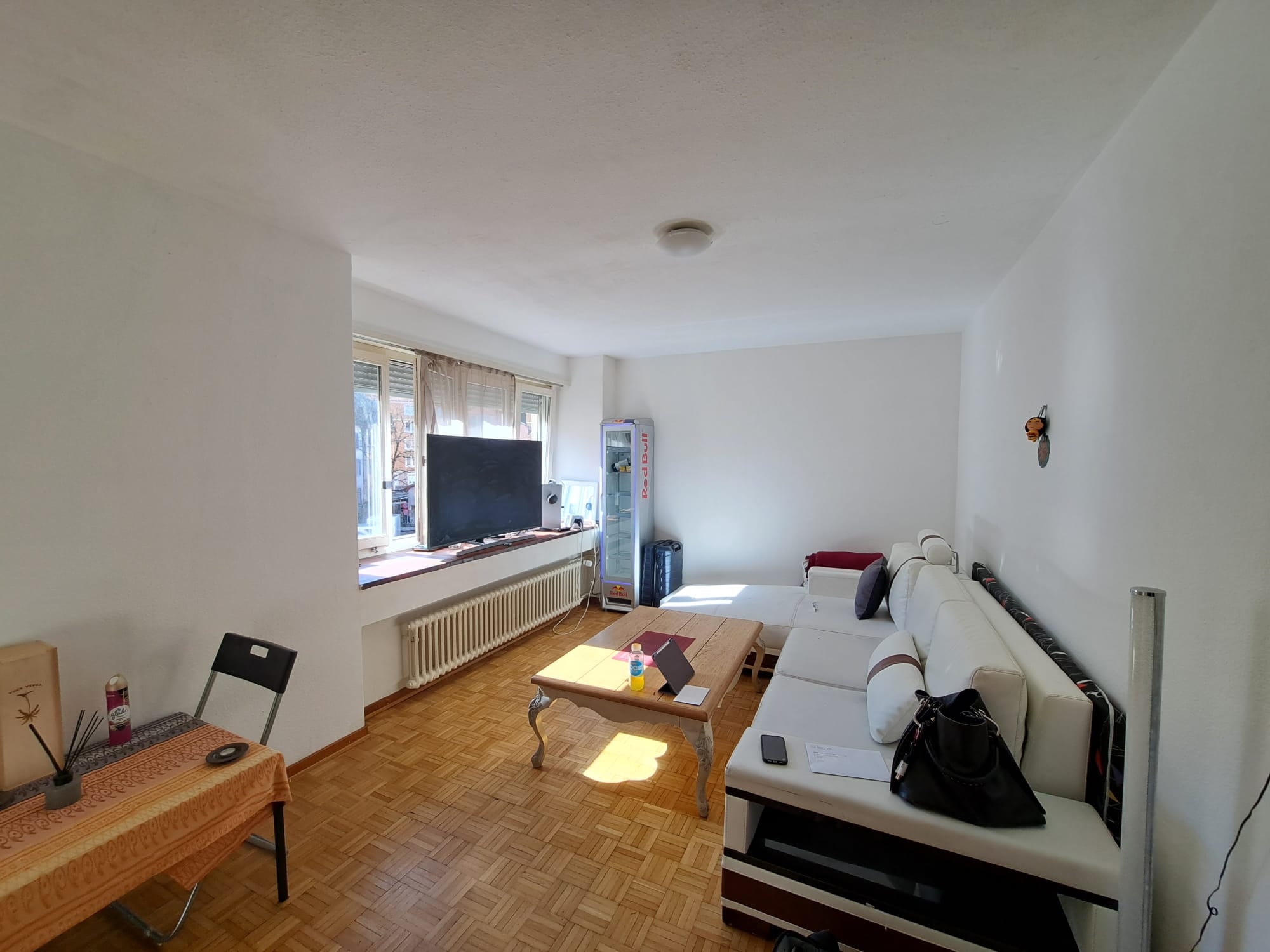 Helles Wohnzimmer mit Balkonfenster und einfacher Möblierung