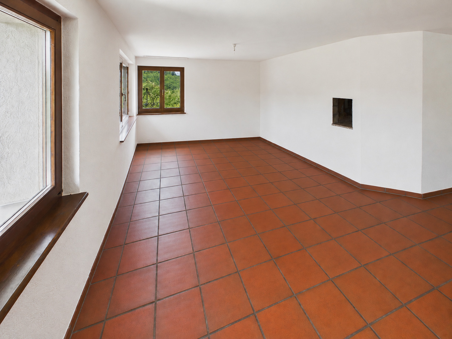 Leerer Wohnraum mit Terrakottafliesen und Holzbalkenfenstern