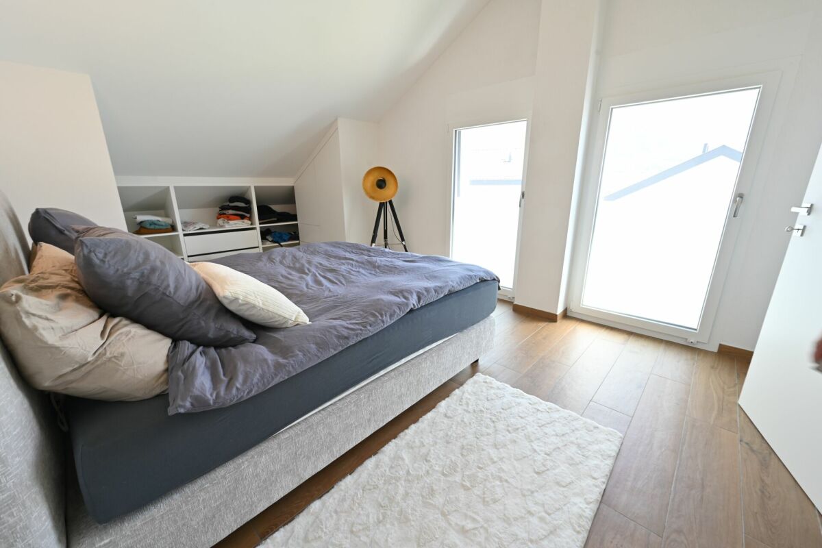 Dachgeschoss-Schlafzimmer mit Bett und großen Fensterflächen