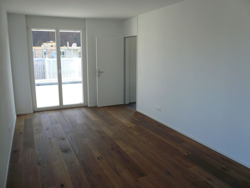 Leerer Wohnraum mit Holzboden und Balkon-/Terrassentür
