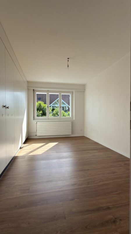 Helles, leeres Schlafzimmer mit Einbauschrank und Blick ins Grüne